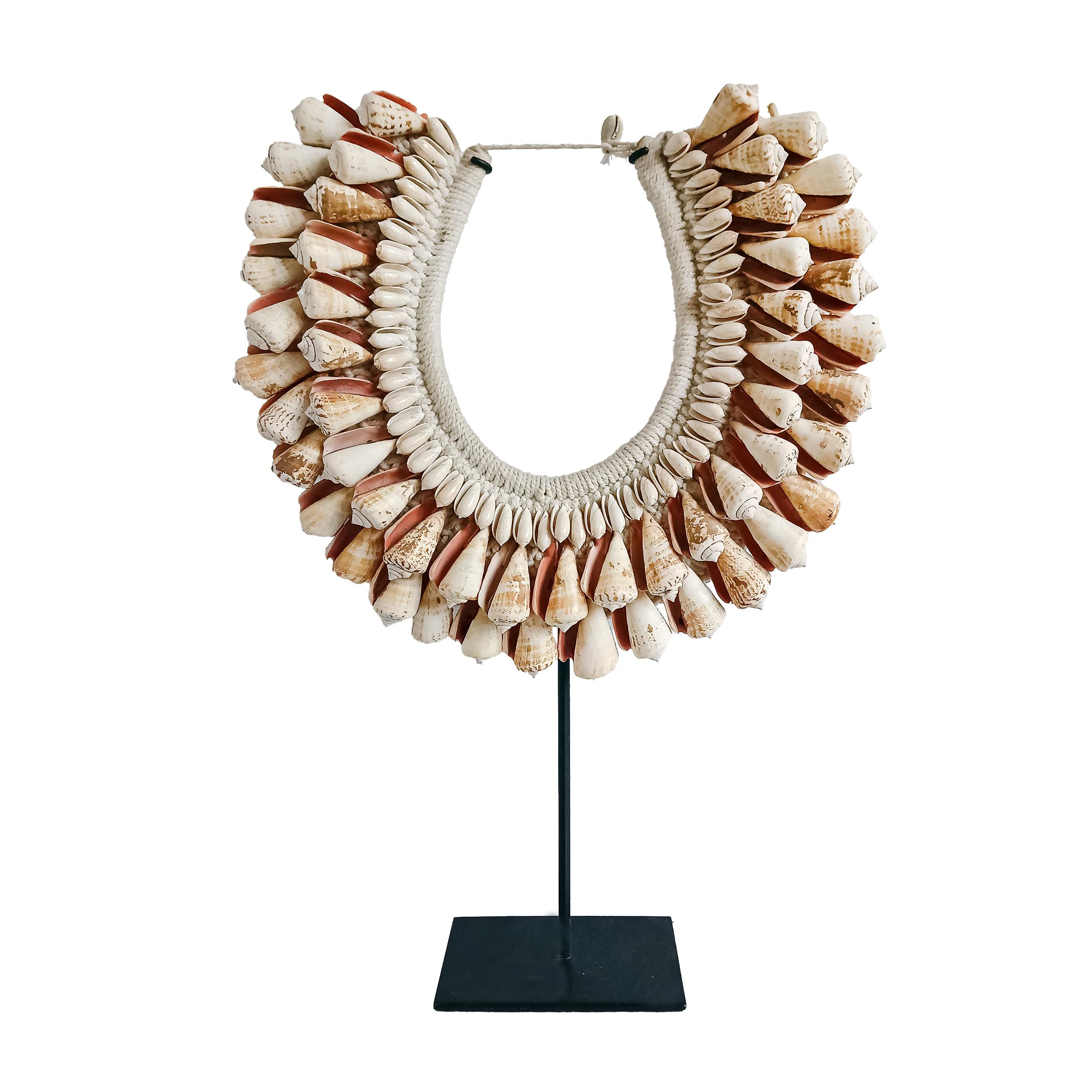A male necklace from the Asmat Village, Papua New Guinea.

 Large cone shells in concentric rows, seamlessly sewn onto a cotton macrame base, which has been hand-knotted around a semi-circular bamboo frame. Mounted on a black metal stand.