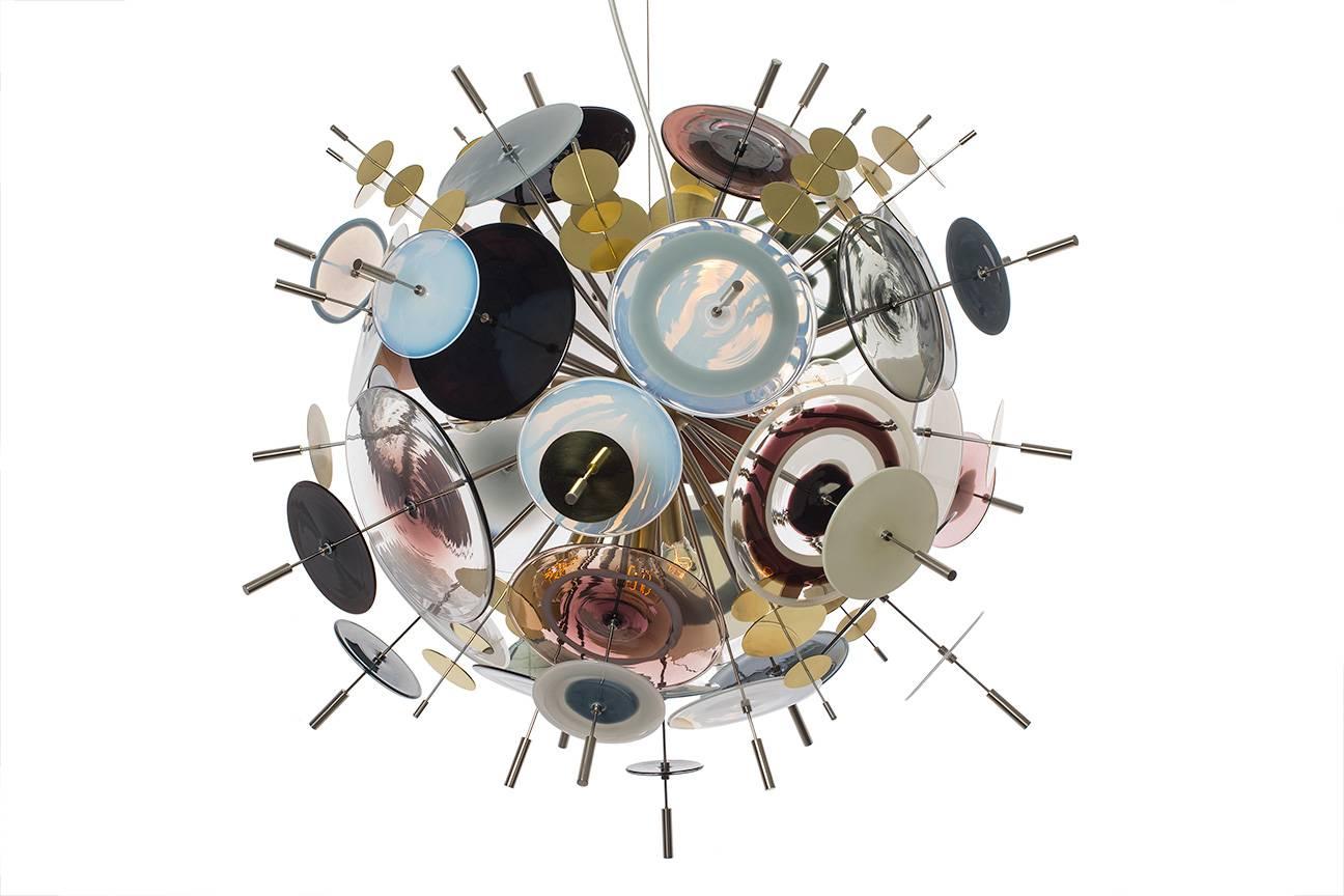 The Confetti glass chandelier features handblown glass discs in a variety of color palates with a choice of metallic accents. Pictured: black, topaz, grey, caramel, ivory, opaline and white. Colors can be selected from existing palates, specified