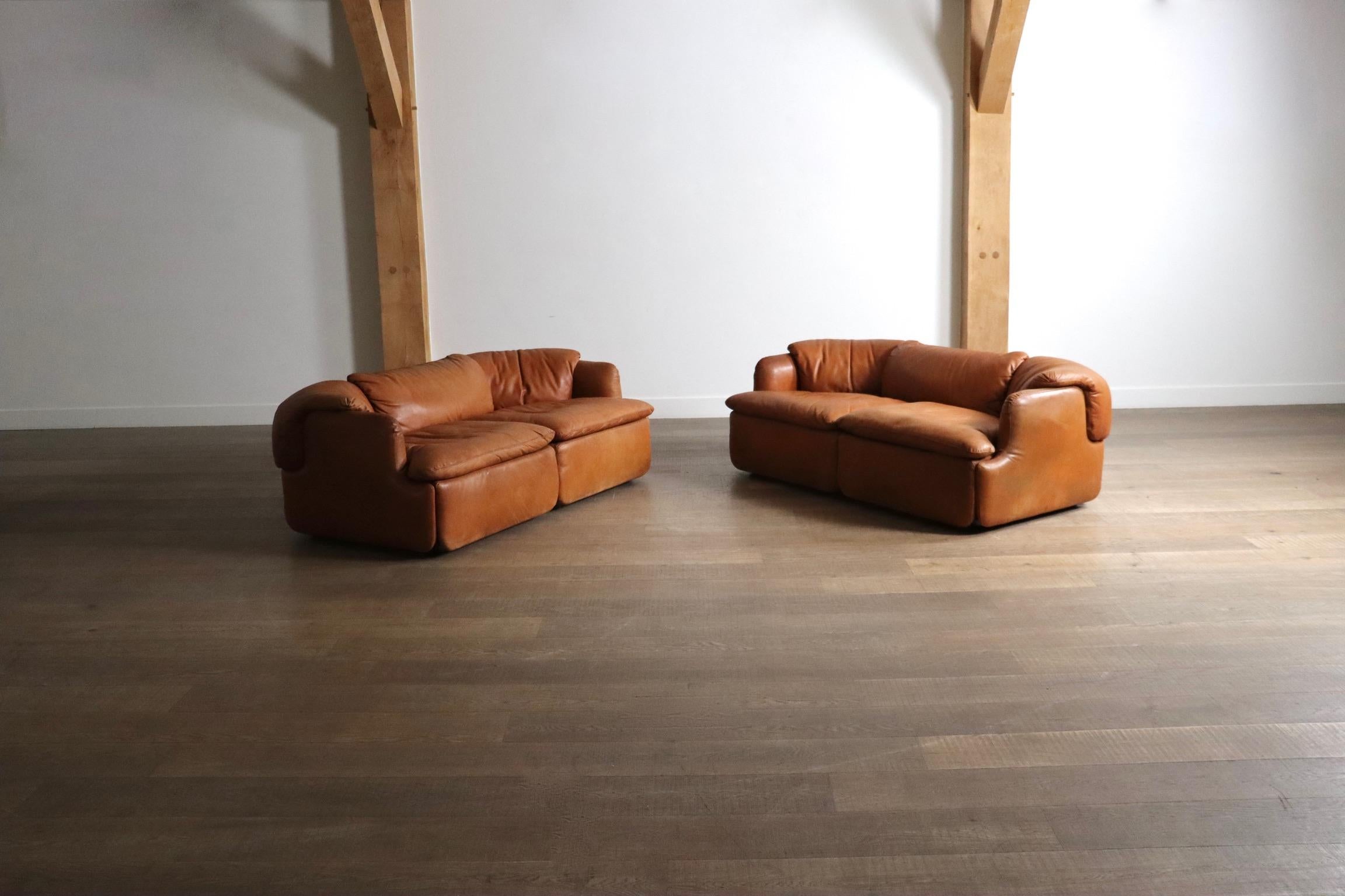 Stunning Confidential two seater sofas in original cognac leather, crafted by renowned Italian architect and furniture designer Alberto Rosselli in 1972 for Saporiti Italia.

This particular pair has its original cognac leather upholstery, which is