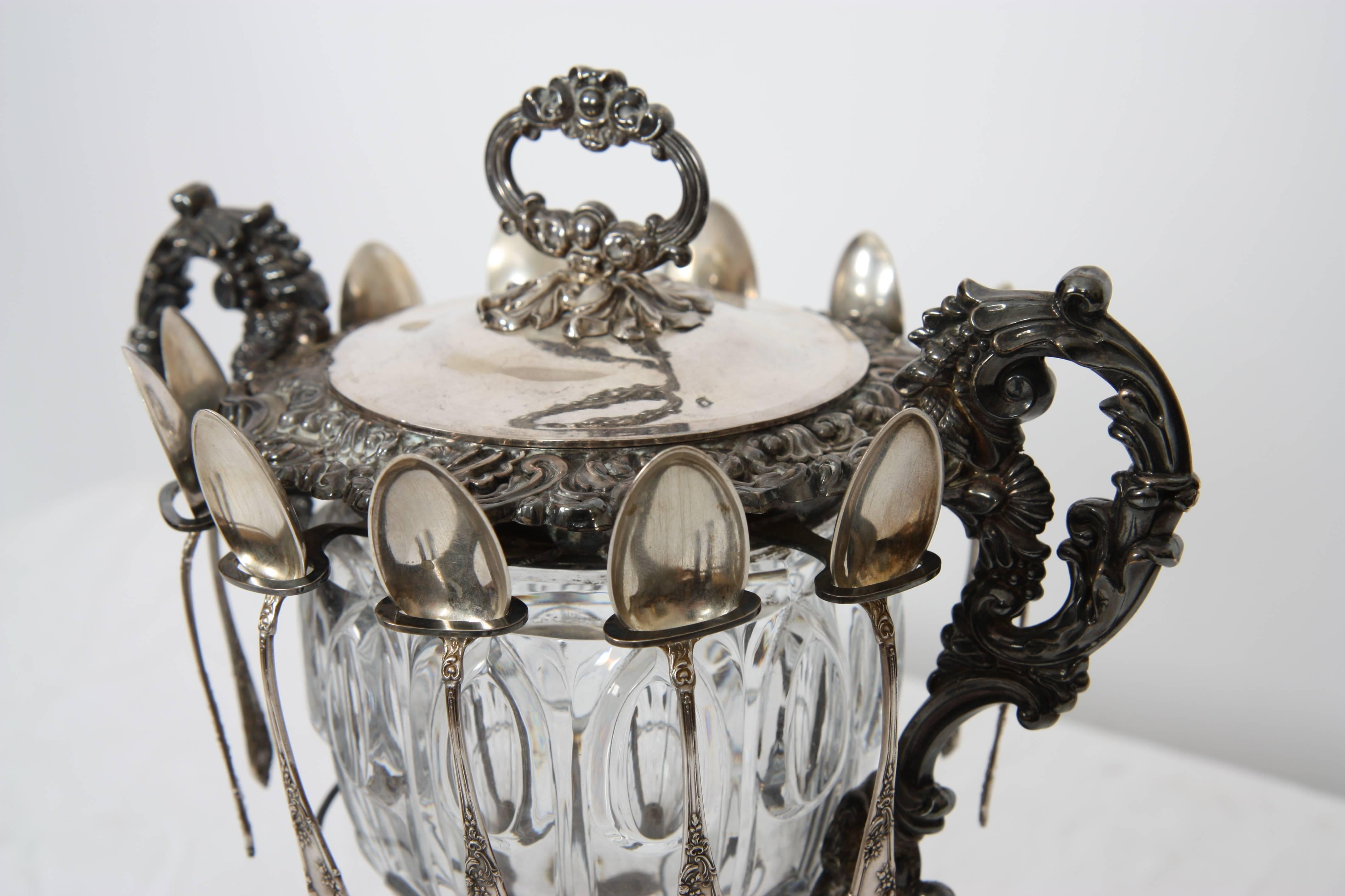 Mounted on a square base decorated with foliage and supported by four rocky feet. The crystal jammer is covered with its lid held by a pair of side handles. Punch of a woman's head. Twelve silver spoons are attached.
Pb: 1.4 kg.