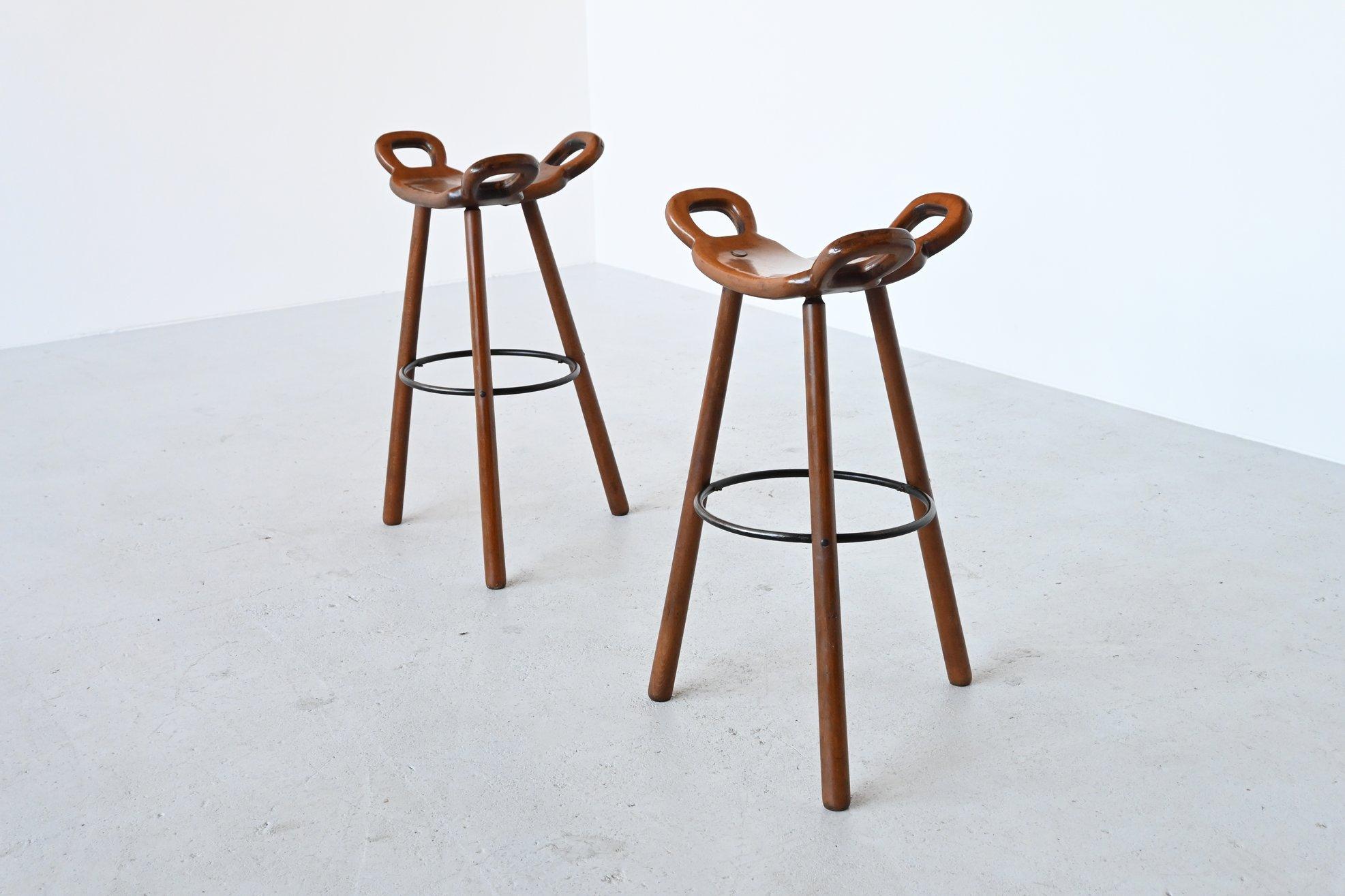 Fantastic pair Brutalist Marbella bar stools manufactured by Confonorm, Spain, 1970. These stools are made of dark stained solid beechwood and they have a solid metal foot rest ring to put your feet on and strengthen the construction. The T-shaped