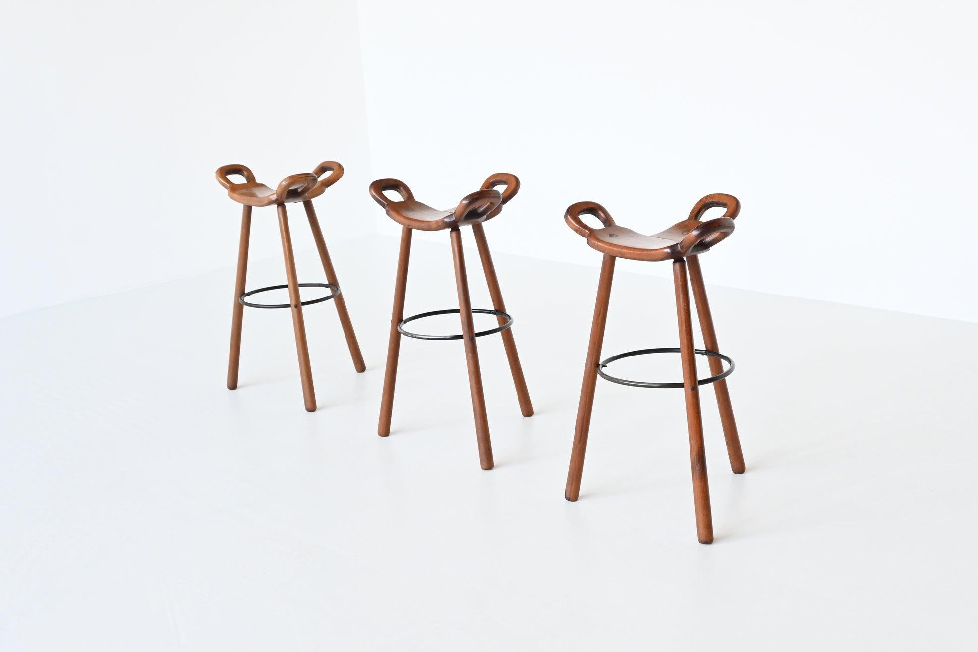 Fantastic set of three brutalist Marbella bar stools manufactured by Confonorm, Spain 1970. These stools are made of dark stained solid beech wood and they have a solid metal foot rest ring to put your feet on and strengthen the construction. The
