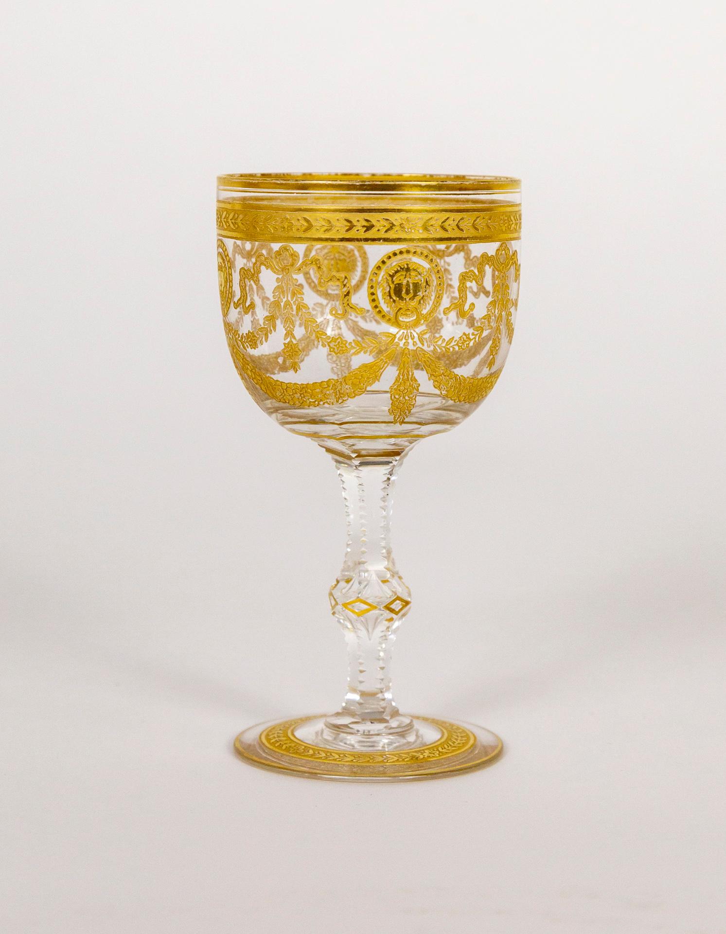 An antique, mouthblown, crystal wine glass, cut and etched, with an intricate gold motif of ribbon, floral garlands, and lion faces. Made by the renowned St. Louis glass company in France in the early 1900s. 4 7/8