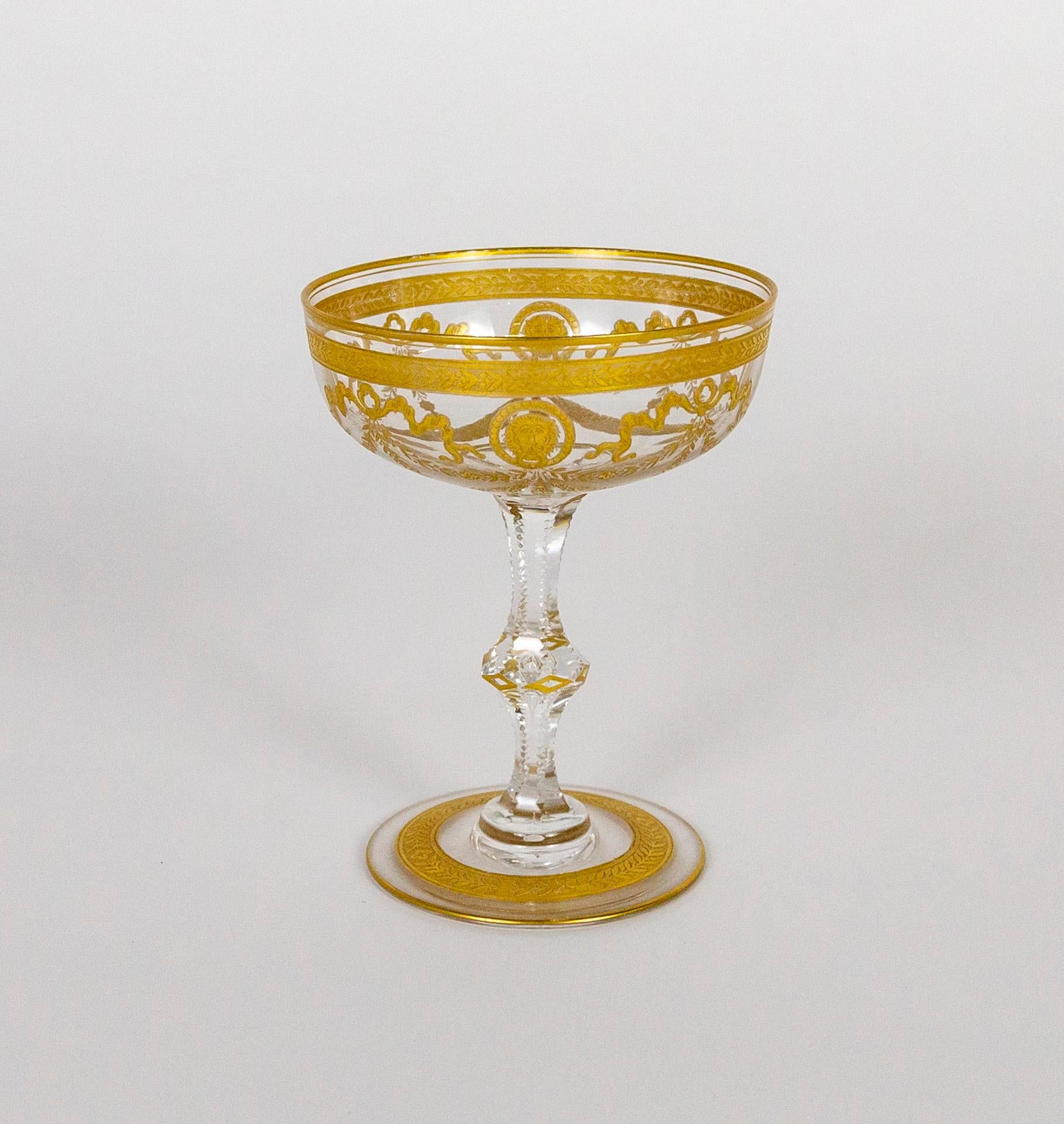 A set of 2, antique, mouth-blown, coupe champagne glasses, cut and etched, with an intricate gold motif of ribbon, floral garlands, and lion faces. Made by the renowned St. Louis glass company in France in the early 1900s. Measures: 4.75