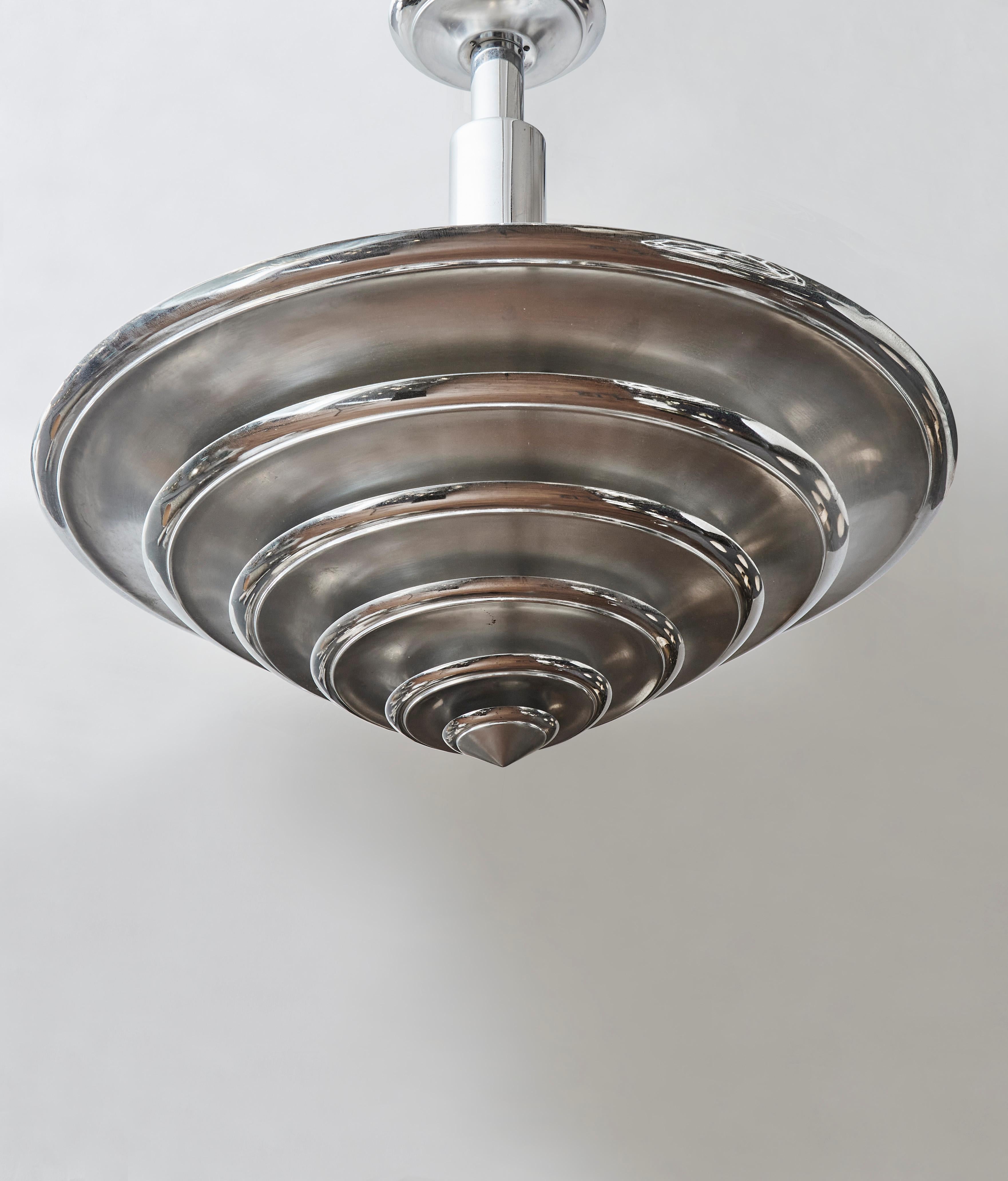 Very nice chandelier made of a central stem and a conical metal shade made of different sized rings.

Three lights inside the cone, enlightening the ceiling and through the rings.