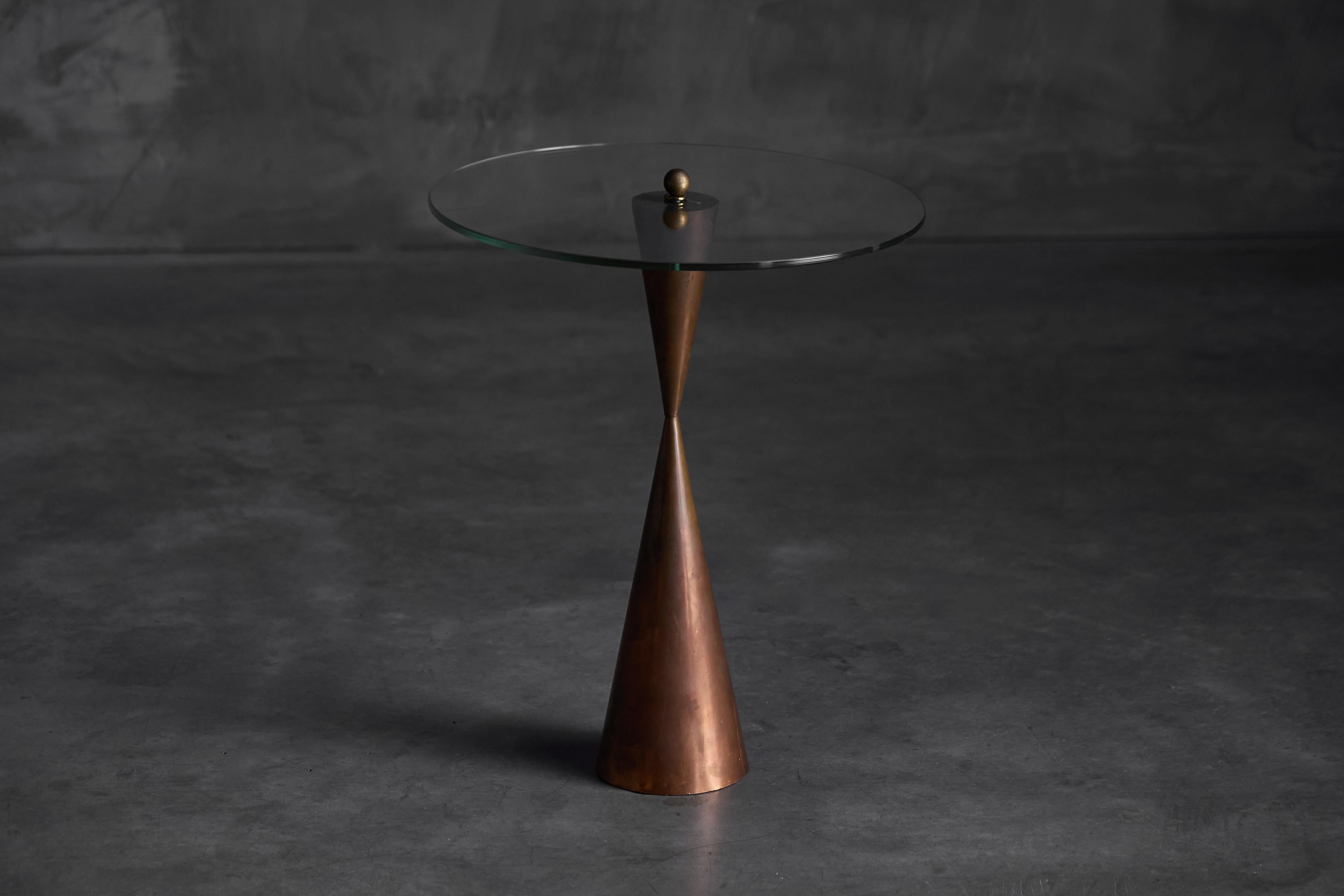 This 1970s conical side table features a sculpted copper base and a clear glass top. The warm patina of the copper contrasts beautifully with the crisp transparency of the glass, creating a refined interplay of materials. With its striking geometric