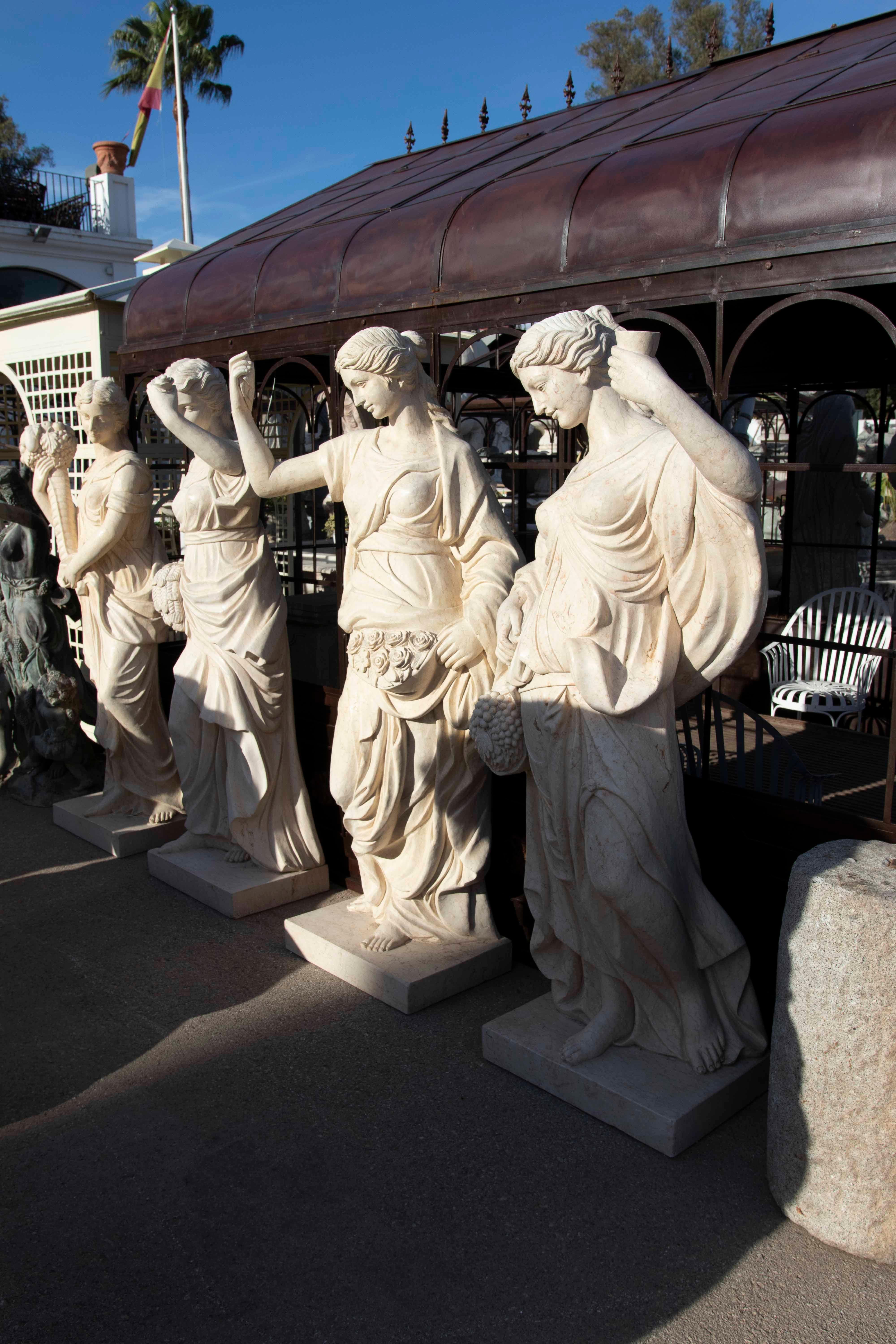 Imponente conjunto de cuatro esculturas en mármol natural representando a las Cuatro Estaciones. Cada figura femenina está tallada con gran maestría, portando atributos simbólicos como frutas, flores y cosechas que evocan la abundancia y el ciclo de