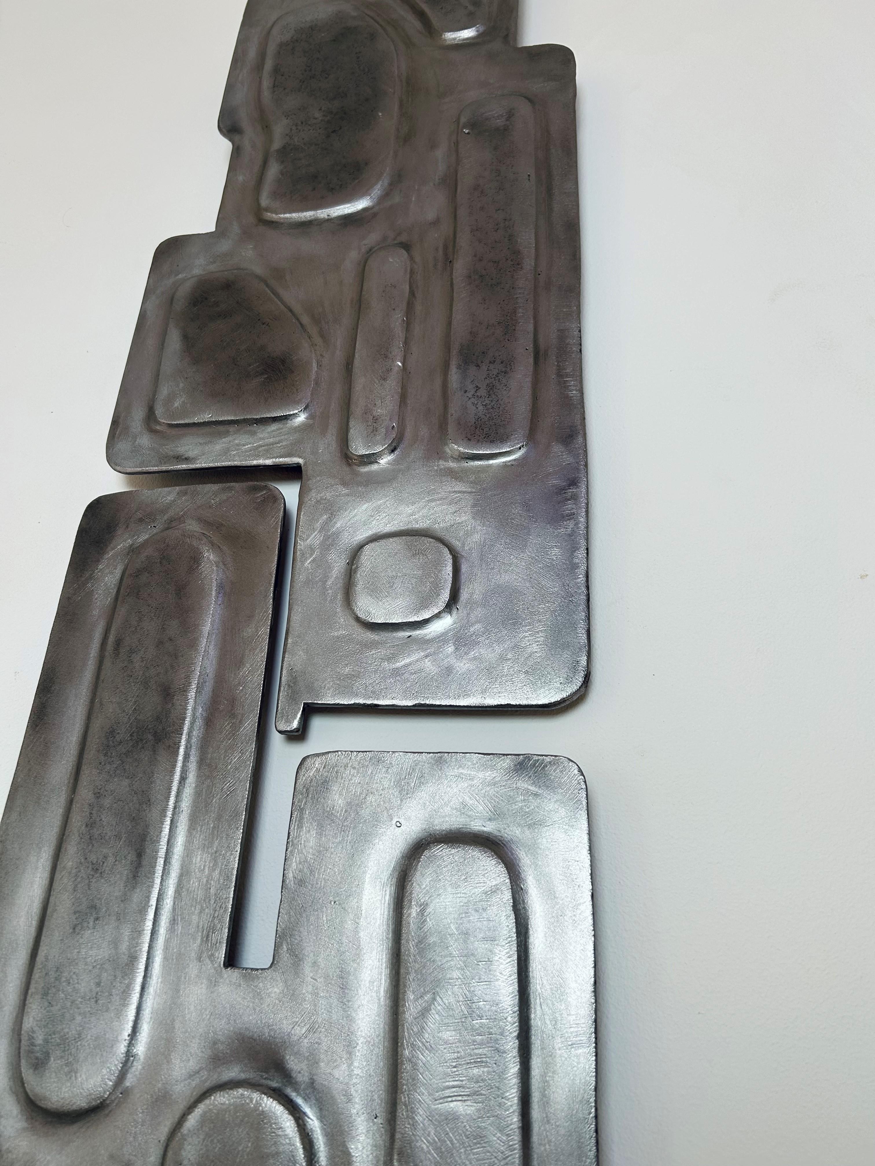 Two panels flowing into one another without touching, each harboring forms that are intrisically connected. A steel wall piece, set slightly off the surface, allowing light to play aross it and cast a delicate shadow. 