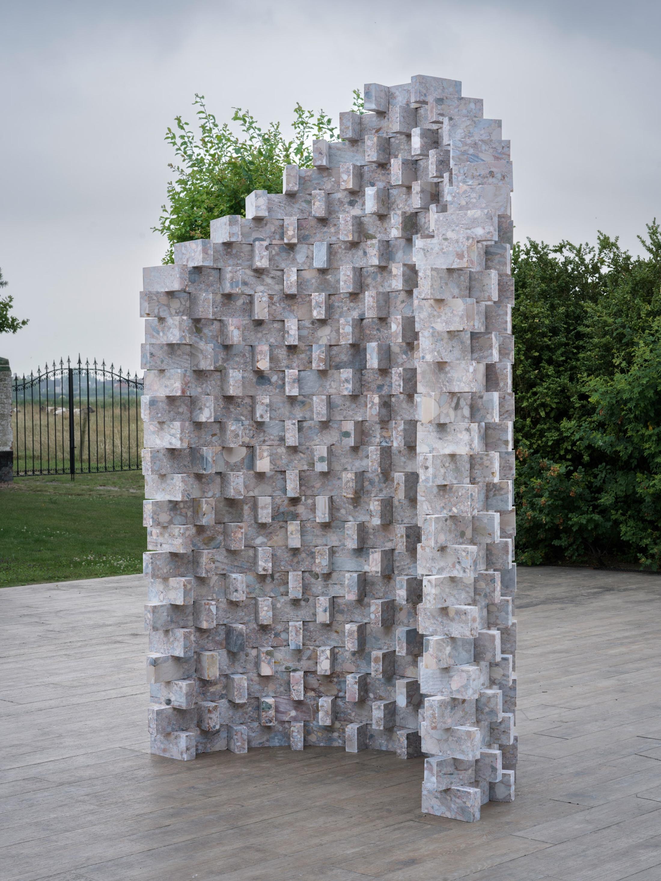 Untitled Column (Timeless Remnants), 2025
Natural stone, 386 bricks

This sculptural column remains unbound, nomadic, and ever-evolving. Its elements are arranged alternately along the length and crosswise, generating a rhythmic interplay of light