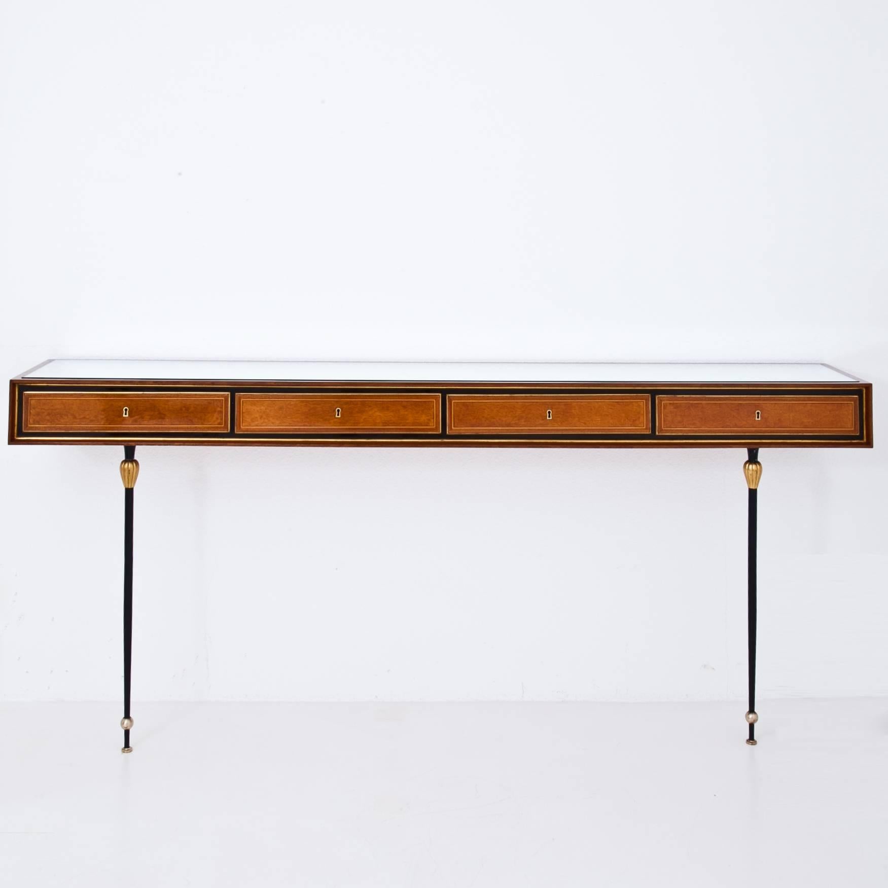 Mahogany console with four drawers on tall slim metal legs. The console is decorated with fine thread inlays on the front and has a mirrored glass pane on top. The fitting chair repeats the same legs and was reupholstered with an elegant black