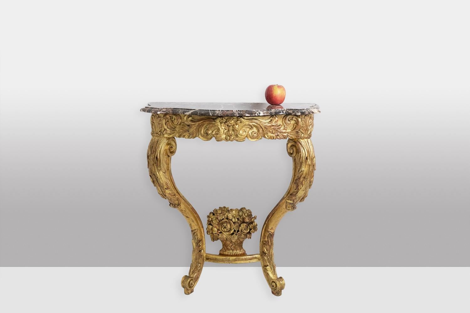Gilded and carved wood console table from the Louis XV period, the curved base and belt decorated with scrolls, acanthus leaves and volutes, and the base joined by a spacer bar with a basket of flowers in the center. Scrolled marble top, gray in