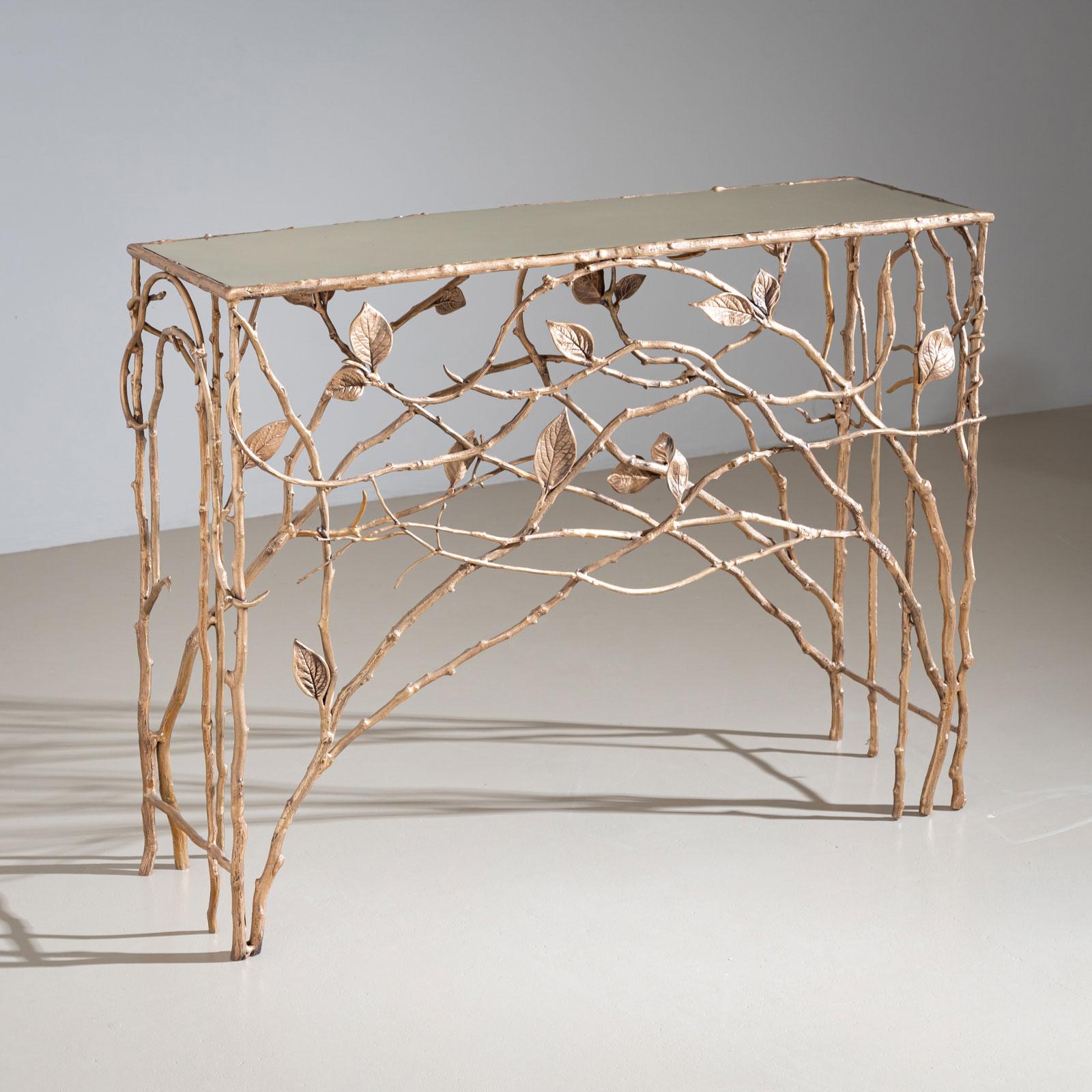 Extraordinaire console en métal conçue sous la forme de branches stylisées ornées de feuilles, formant une silhouette arquée. Le design naturaliste est remarquablement contrasté par sa finition dorée, tandis que le plateau en verre doré encastré