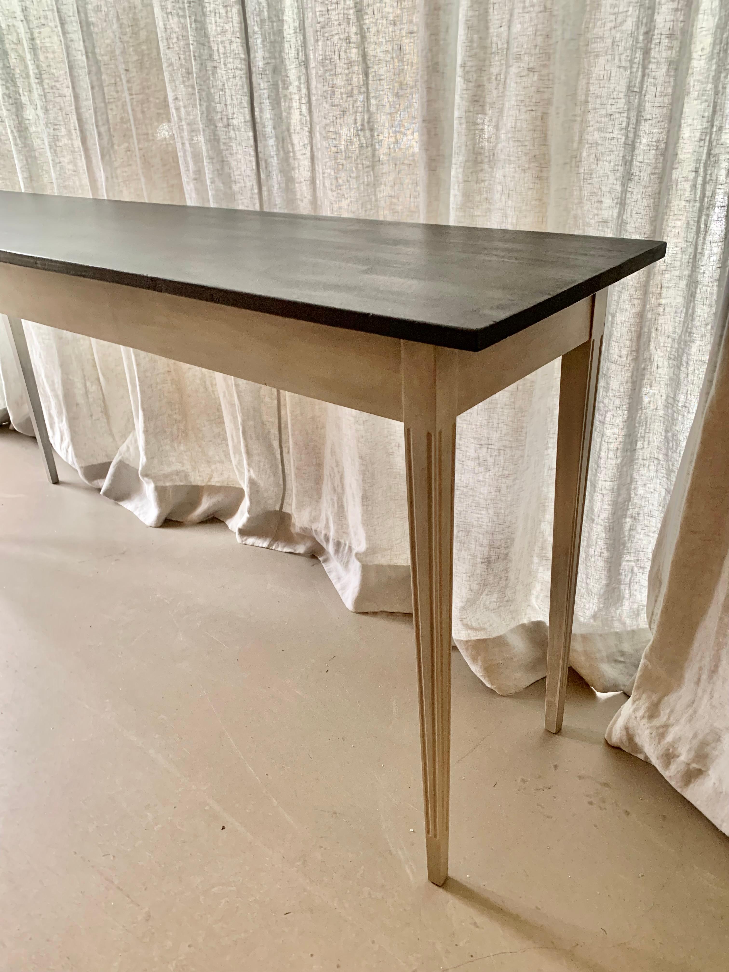 Graceful and long Gustavian style console table with grey patinated elegantly tapered legs with vertically carved details and a black painted table top. Great for the large hallway or living room.
