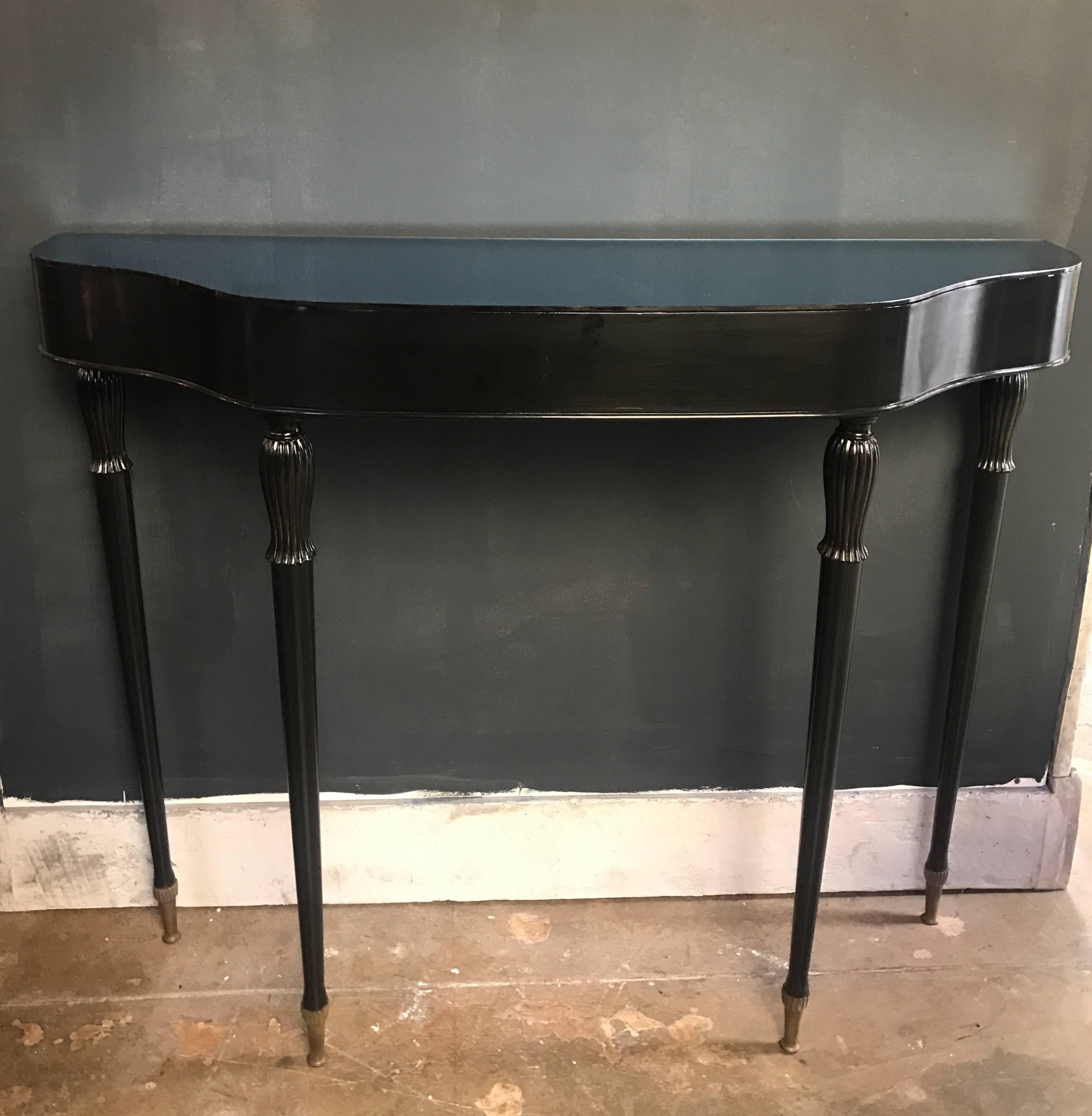 A midcentury Italian console table with black finish and deep blue mirrored glass top.
Elegant clean lines with tapered legs and unique brass footing.