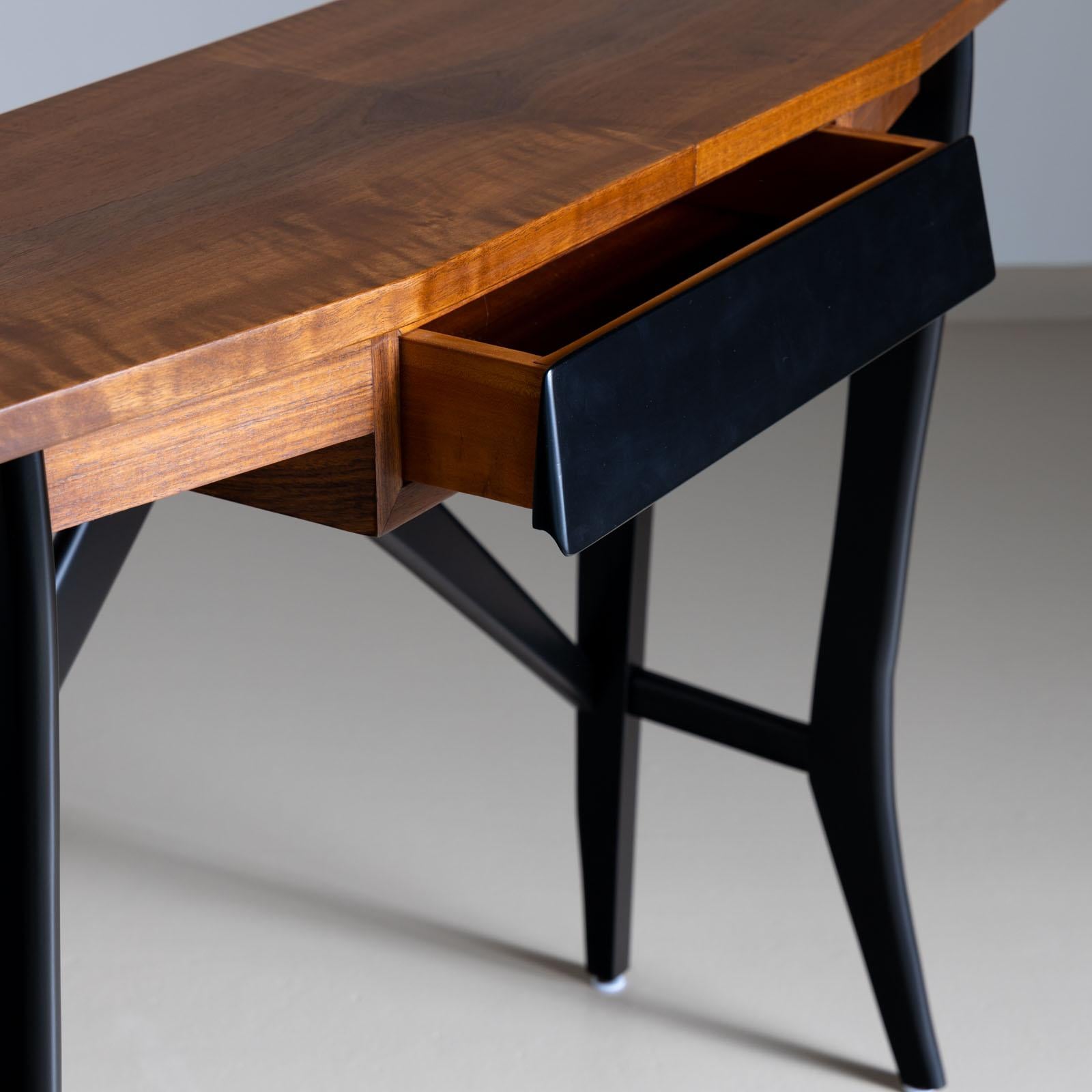 The console table boasts a walnut veneered tabletop complemented by an ebonized frame, mirroring the design of the drawer front. With one drawer for added functionality, this piece has been meticulously restored and hand-polished to showcase its