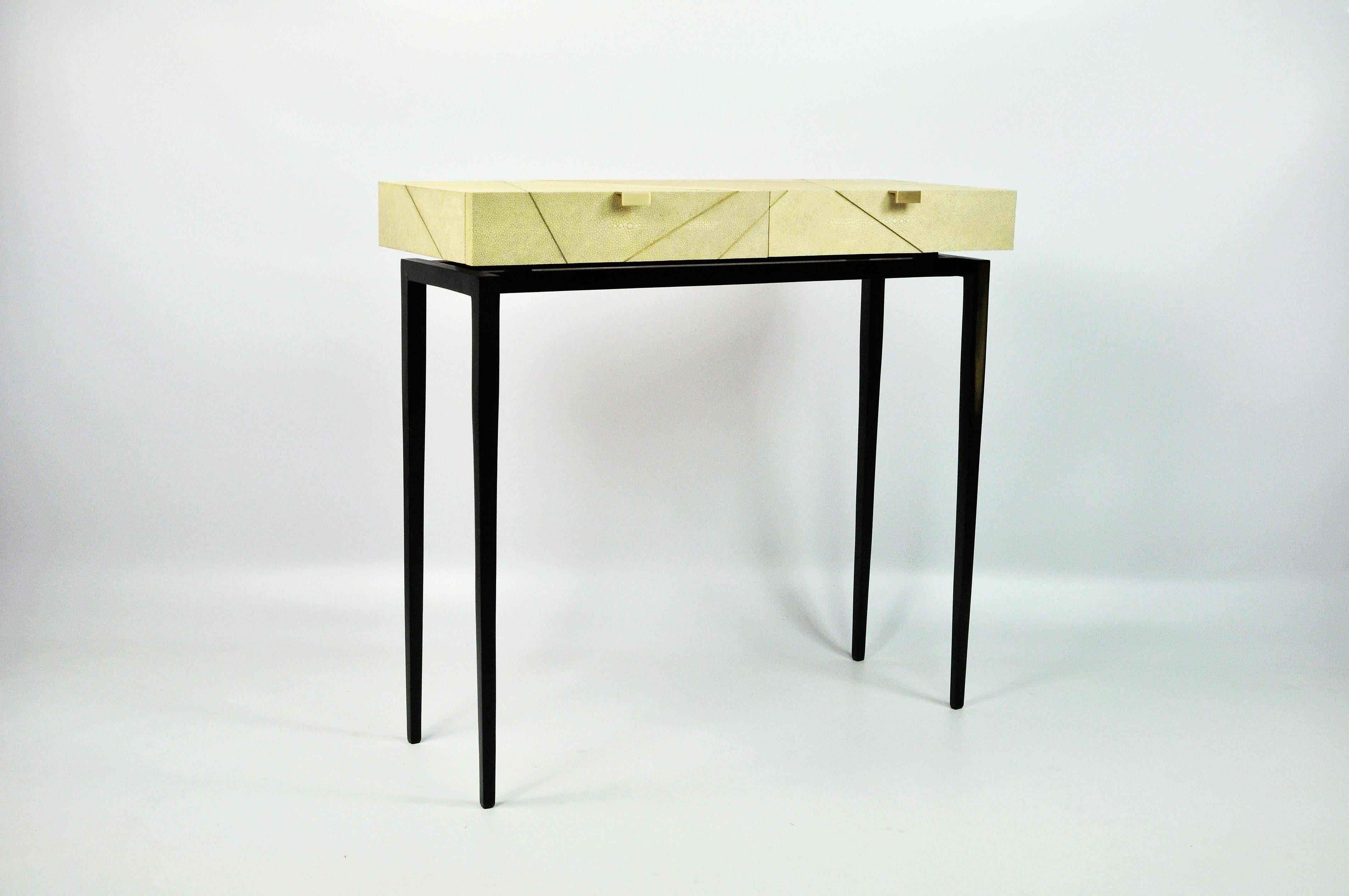 La table console RADIUS est fabriquée en galuchat véritable avec des garnitures en laiton.
Il comporte deux tiroirs fins et les pieds sont en métal peint en noir satiné.
Cette pièce s'installera très bien dans votre entrée ou votre salon. Ses