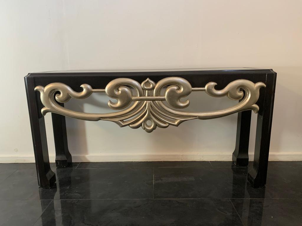 Eclectic console table, 1980s. Black lacquered wood structure with sober lines reminiscent of Art Deco style and imposing central silver Baroque fragment. 
Packaging with bubble wrap and cardboard boxes is included. If the wooden packaging is needed