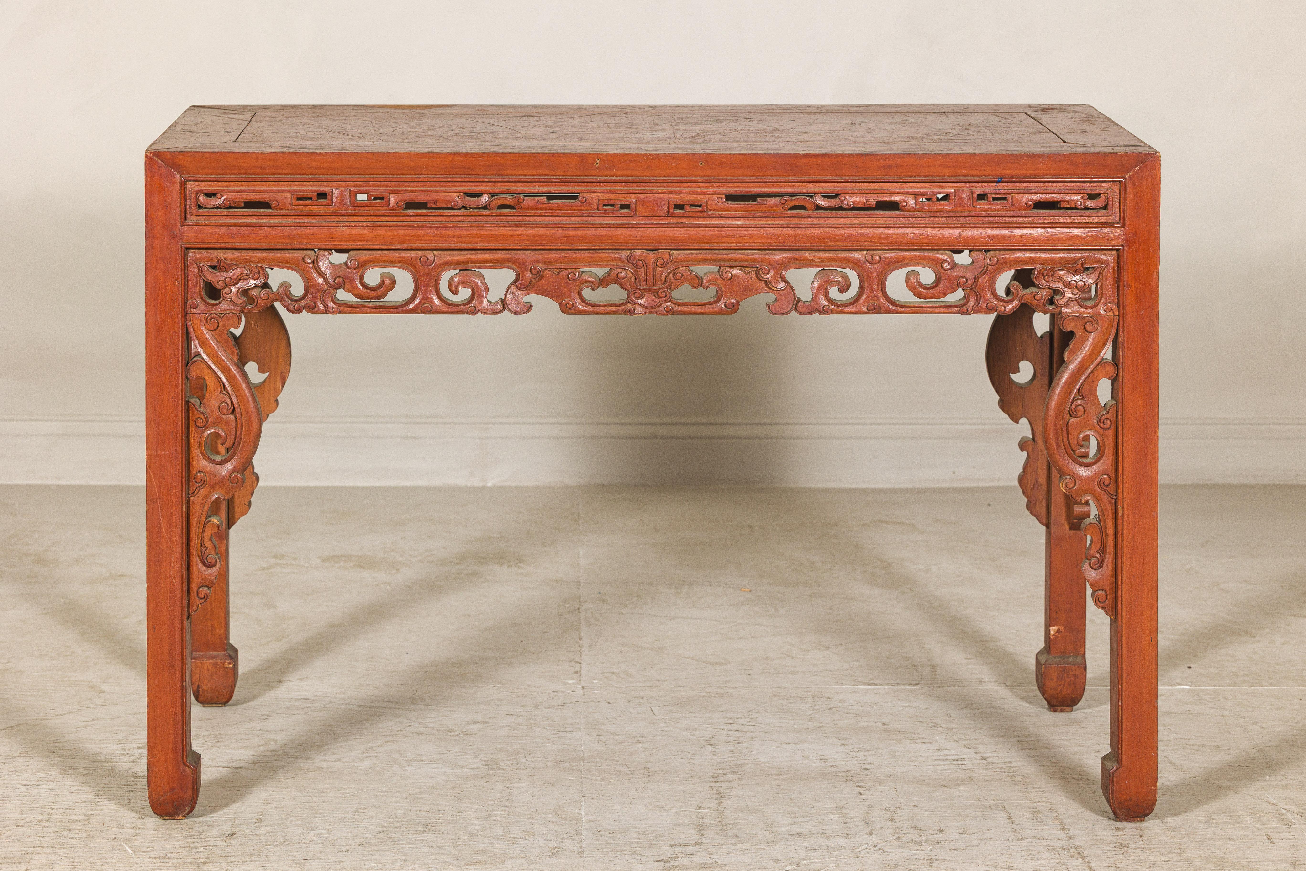 A refined Chinese console table with a cinnabar-toned lacquer finish and intricate openwork carving along the waist and spandrels, likely dating to the late Qing Dynasty period, circa early 20th century. Crafted from jumu (elm wood), the table