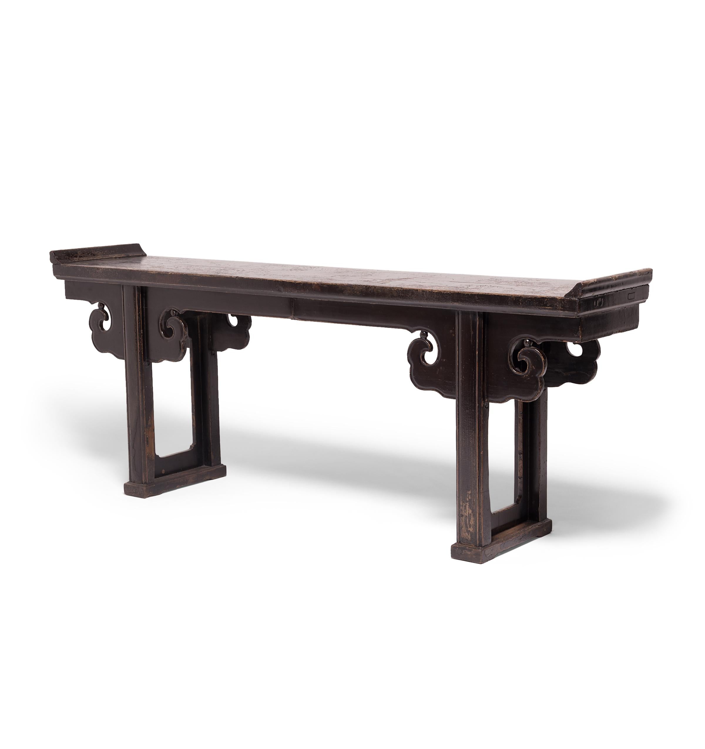 Created in China's Shanxi province in the early 19th century, this impressive altar table with everted ends features straight legs joined with a base stretcher, topped by hand-carved spandrels resembling billowing clouds. Constructed with