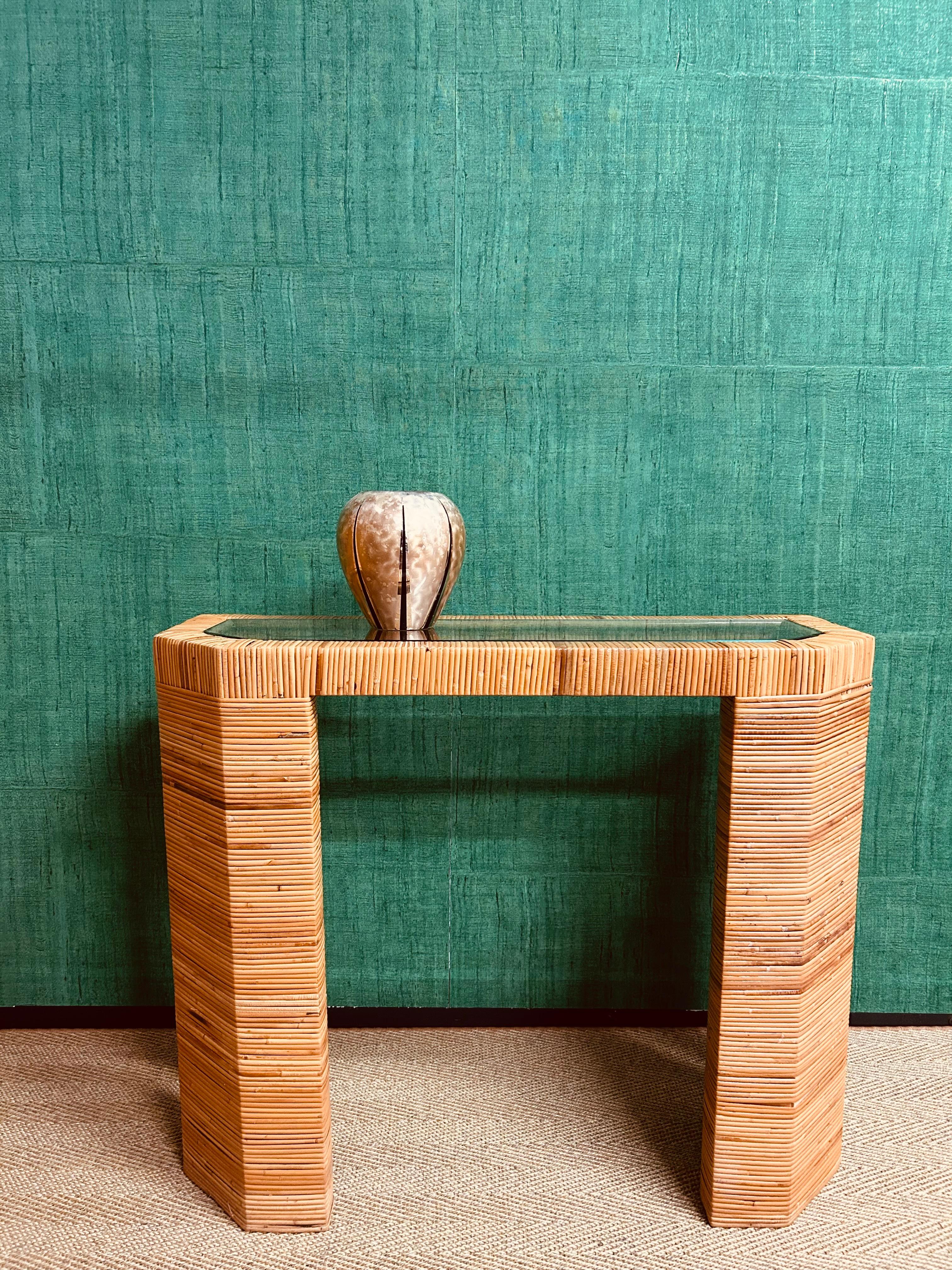 Beautifully designed and expertly made, this wicker wrapped console table is a delight to behold!

The substantial cuboid shape in almost brutalist fashion, is alleviated by the open sides and the cut front corners, which are mirrored in the glass