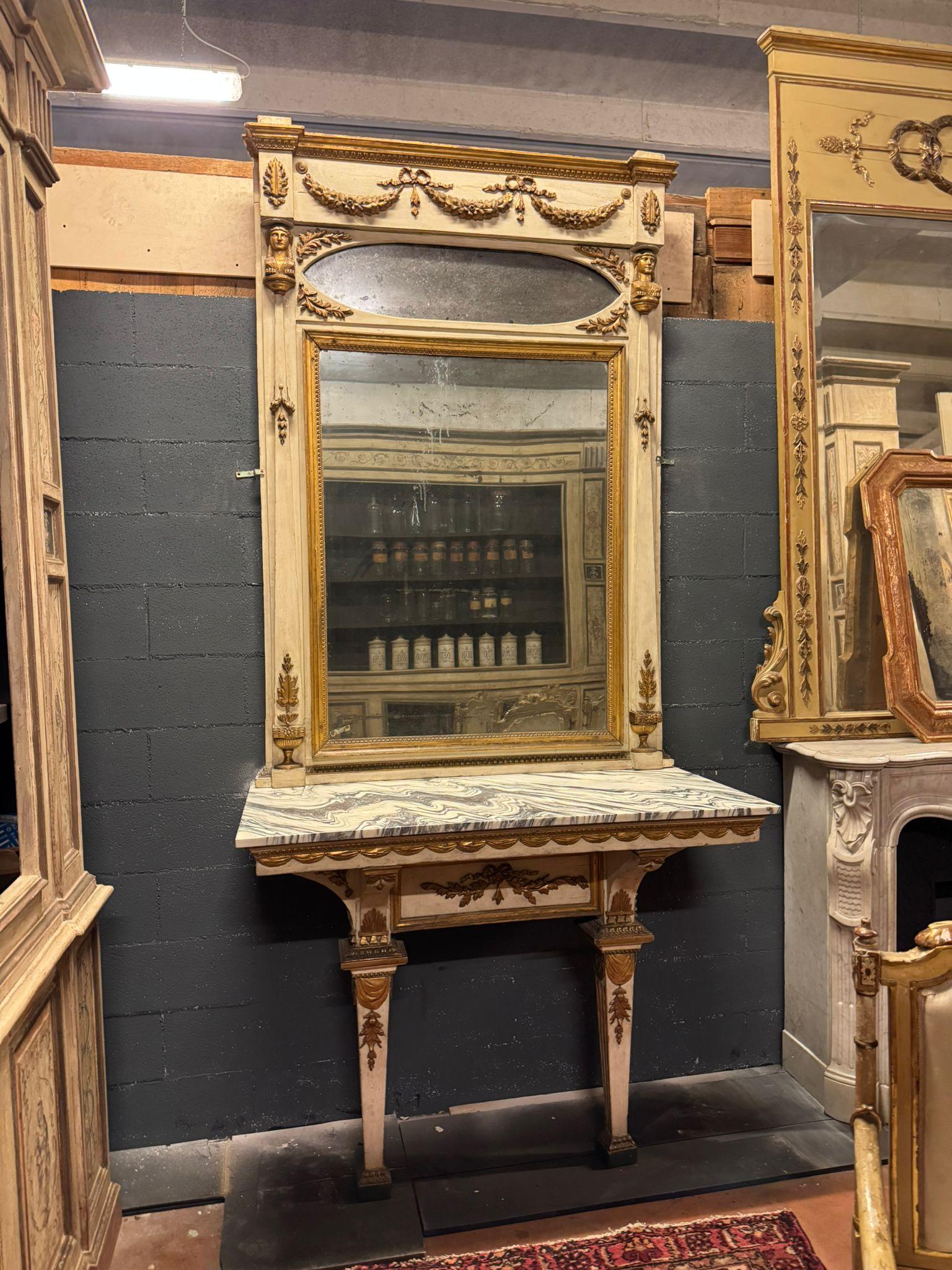 Consola antigua formada por una mesa mural y un espejo sobre ella. Este conjunto de estilo neoclásico presenta una base lacada y frisos dorados, una encimera de mármol blanco con hermosas vetas negras, un espejo contemporáneo y ricos adornos por