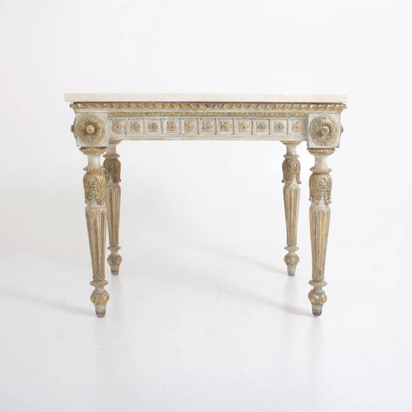 Console table on four fluted conical legs with grey and gilt paint and carved floral ornaments. The white stone top was added later.