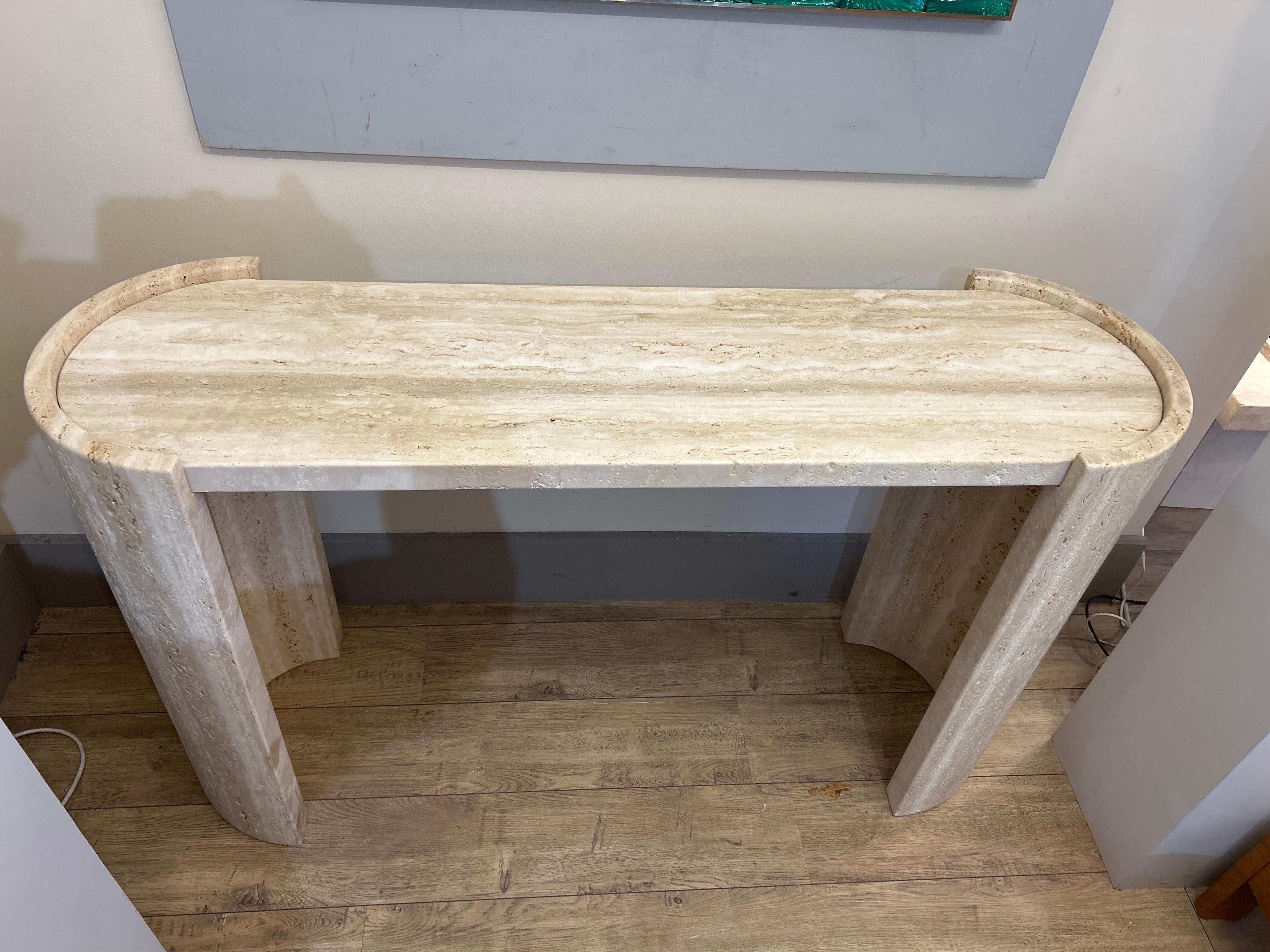 La consola es de piedra natural (travertino).

Piedra natural (travertino), reconocible por su textura porosa y sus tonos beige y crema.
Es rectangular con extremos redondeados: las dos patas están formadas por elegantes curvas, que añaden un toque