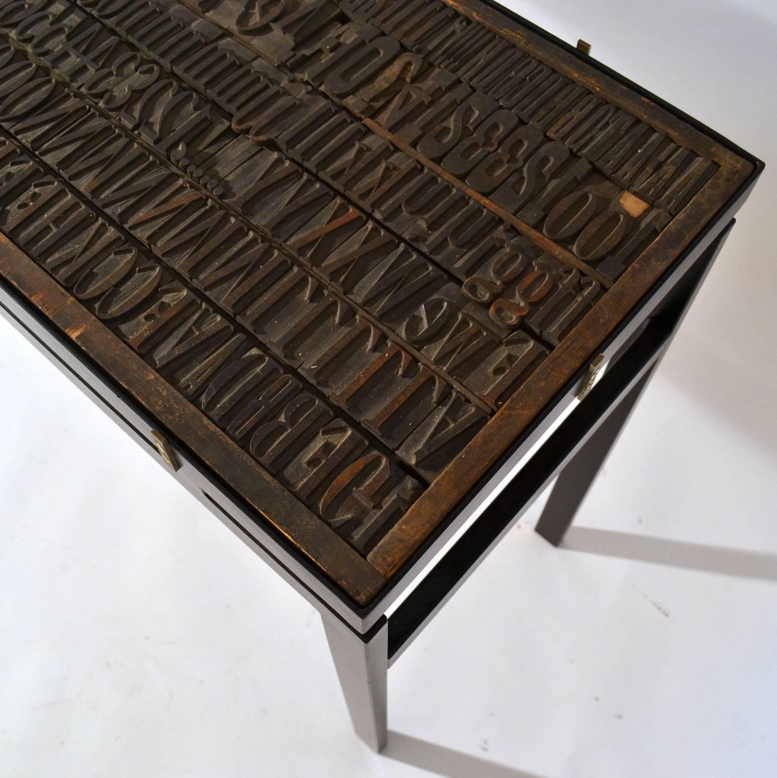 Consola con relieve de letras impresas y tapa de cristal sobre marco de metal negro Madera en venta