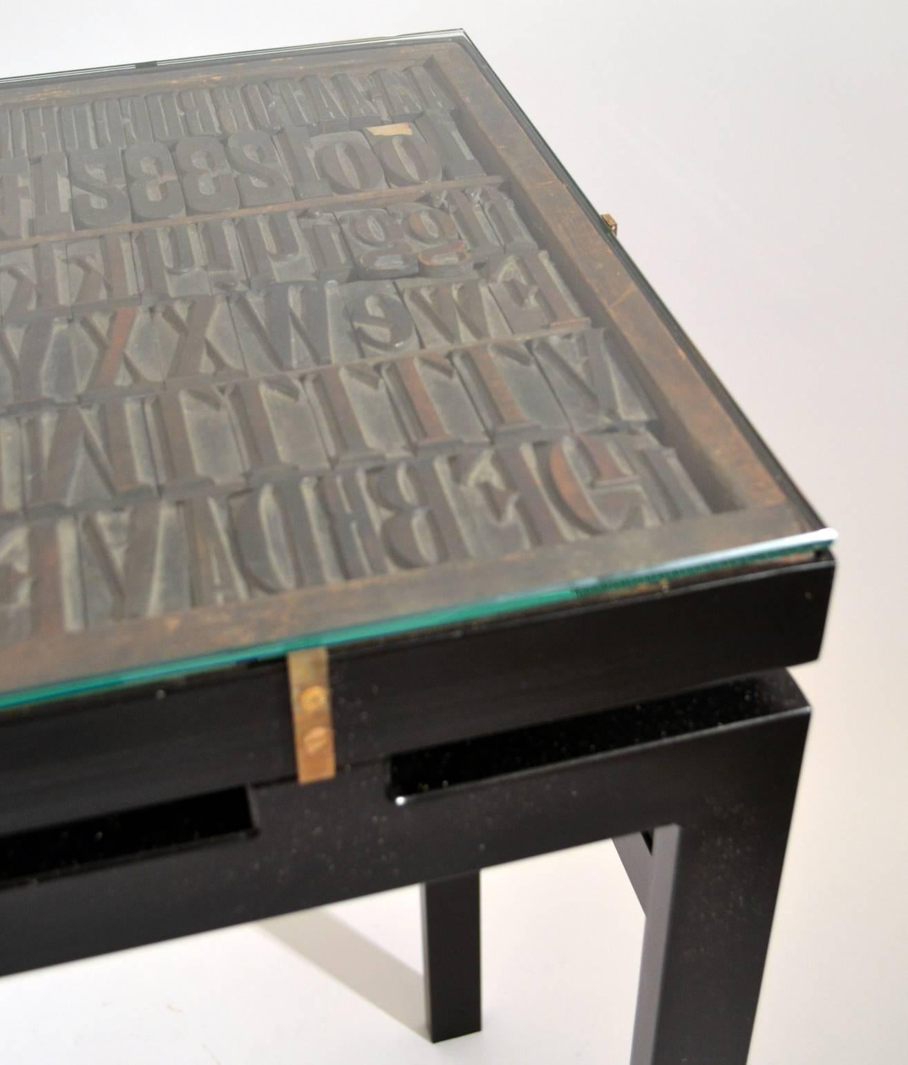 Console with Antique printing letters and glass top on metal frame. The console is specially designed to display 1920's typography letters housed in its original wooden typesetter tray with a variety of wooden vintage letterpress printing blocks of