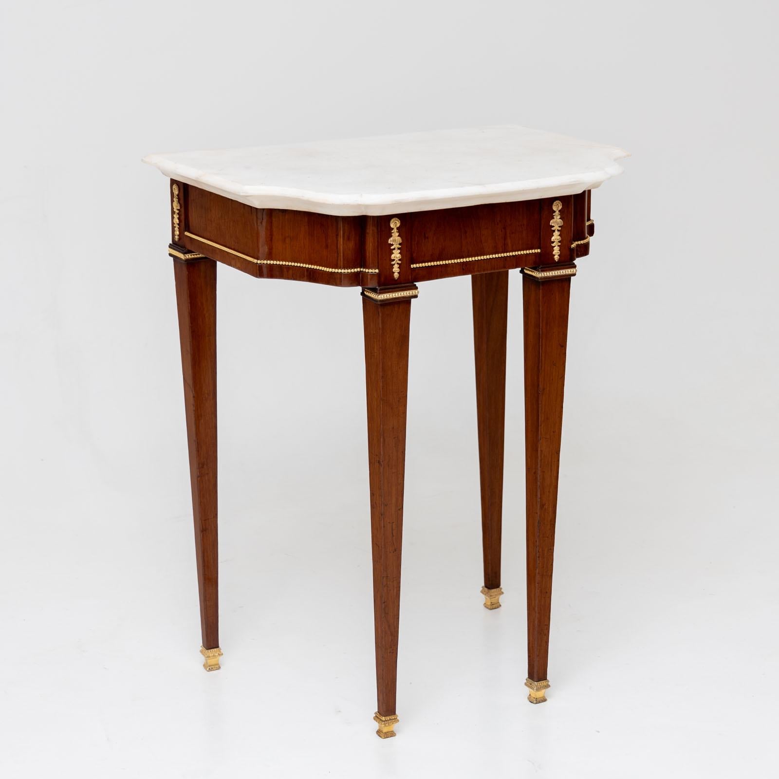 Neoclassical console table with white marble top and gilded applications. The console stands on tall, slender square legs with brass sabots. It is veneered in mahogany and has been professionally refurbished and polished.