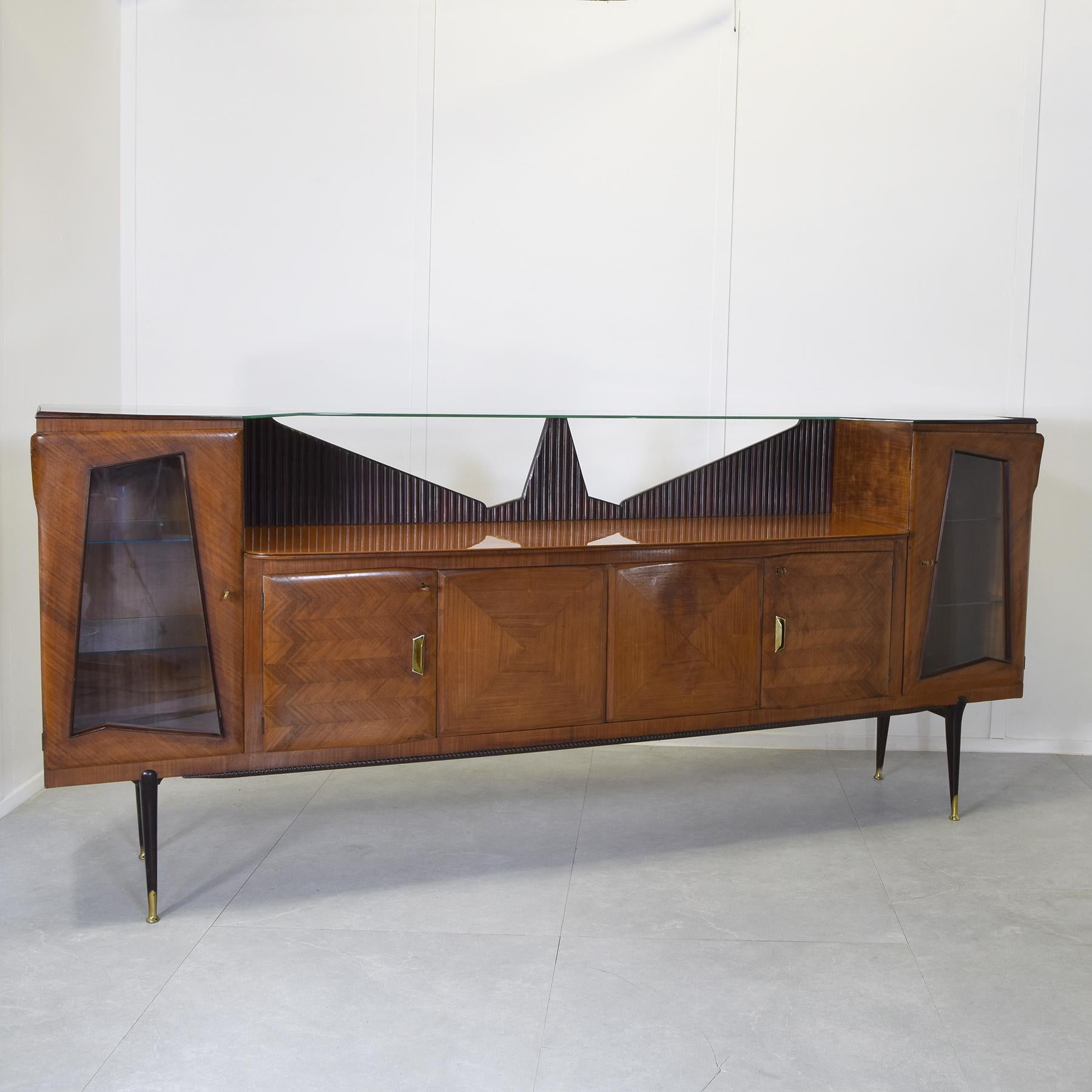 Buffet en bois plaqué palissandre avec pointes en laiton, plateau en verre coloré et cristal, épaulement en bois nervuré et miroirs biseautés, fabriqué par Consorzio Esposizione Mobili Cantù dans les années 1960.


Caisse sur demande pour connaître