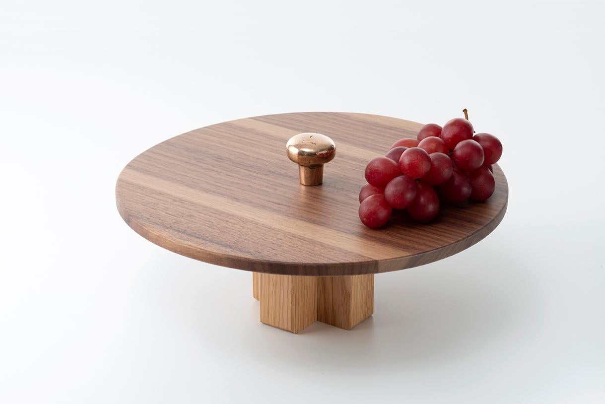 Constantin centerpiece is a simple and useful stand for the table.
The base is in solid oakwood stained black with a cross shape; the round top ø 30 cm is in Canaletto walnut. On the top a bronze handmade handle with an ergonomic bean shape. It is