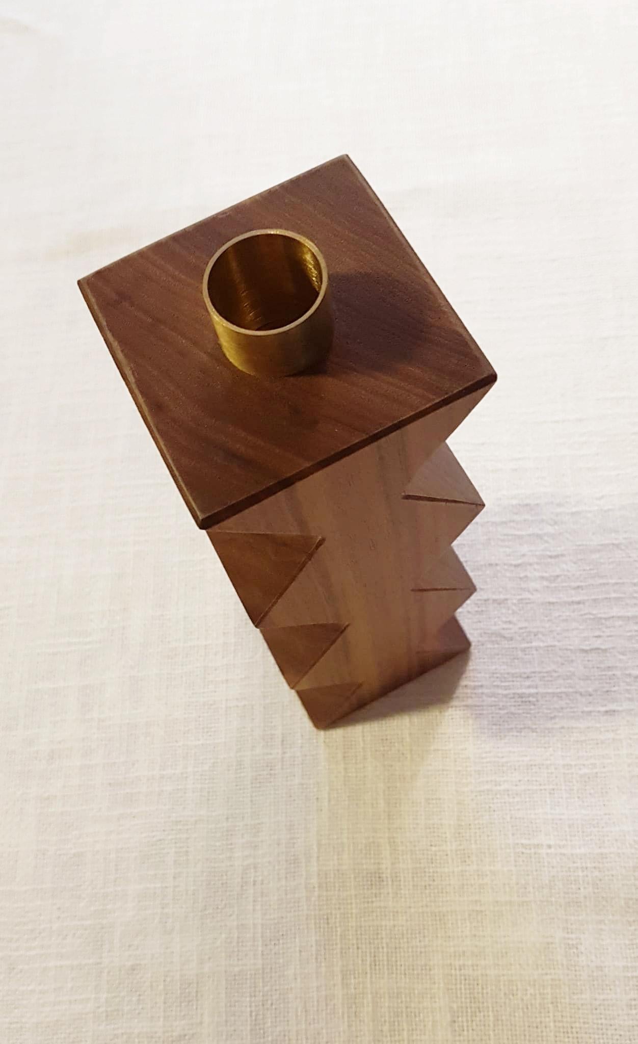 Constantin is a simple but charming candleholder with a geometric shape. The body of Constantin I is in solid oak painted black shaped with a cross, Constantin III in Canaletto walnut shaped with rhombus. The cylinder in natural brass on the top is