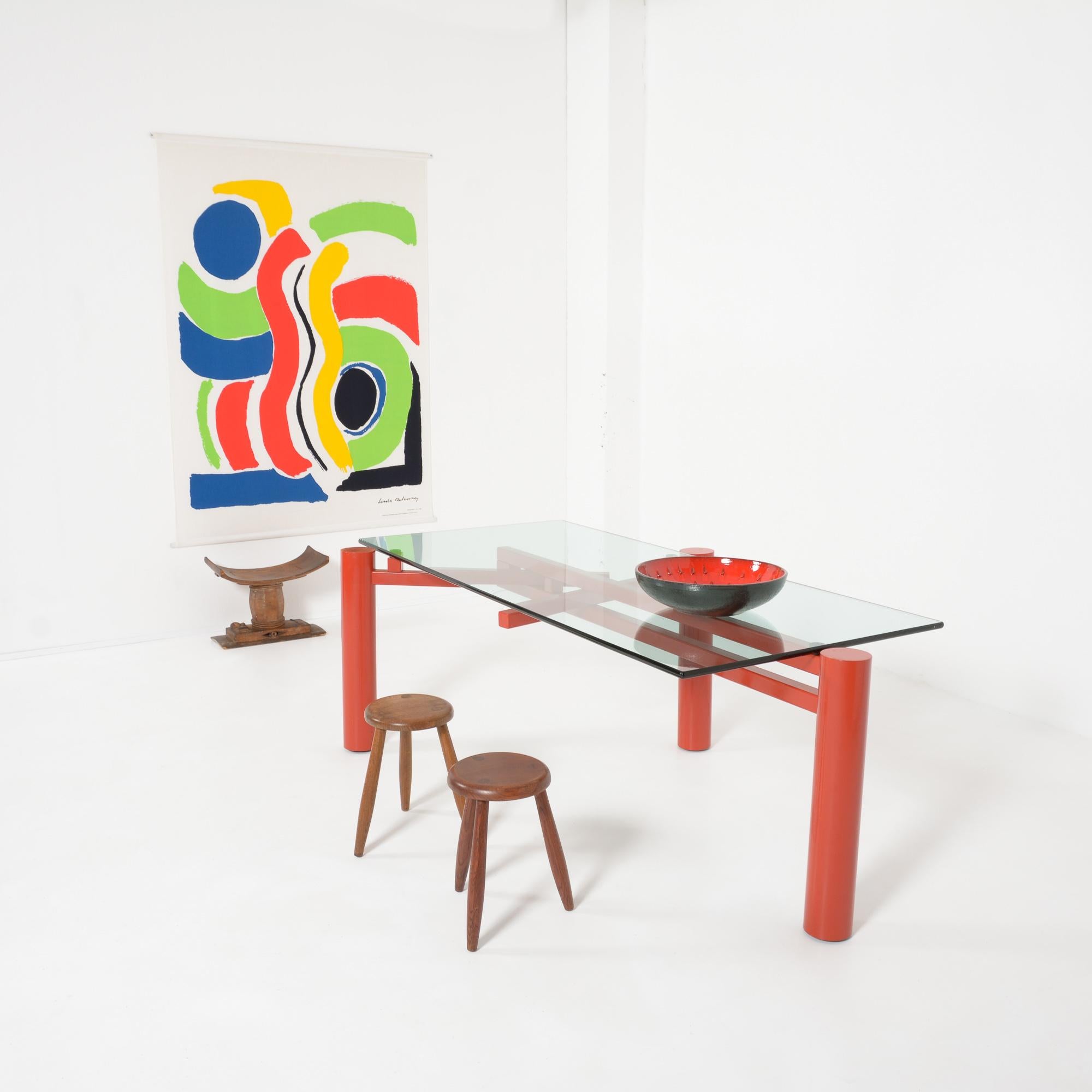 This constructivist dining table was designed by Christophe Gevers and edited by be.classics in 2001.
The heavy red-orange metal base consists of 3 legs that can be placed in different positions so that the rectangular glass top can be changed into