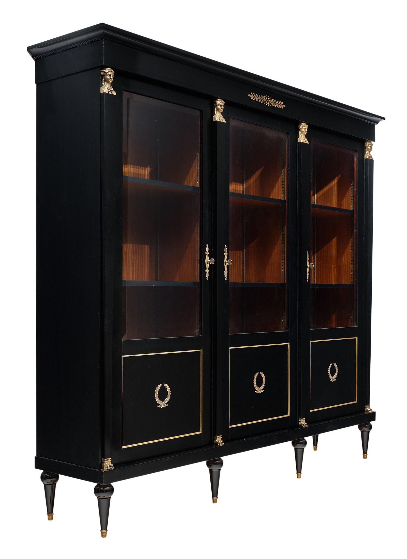 Consulat style French antique bookcase from Lyon; France. This Consulat / Empire style piece is made of solid mahogany that has been ebonized and finished with a lustrous museum quality finish. The gilt bronze decor of “cariatides”; laurel wreaths;