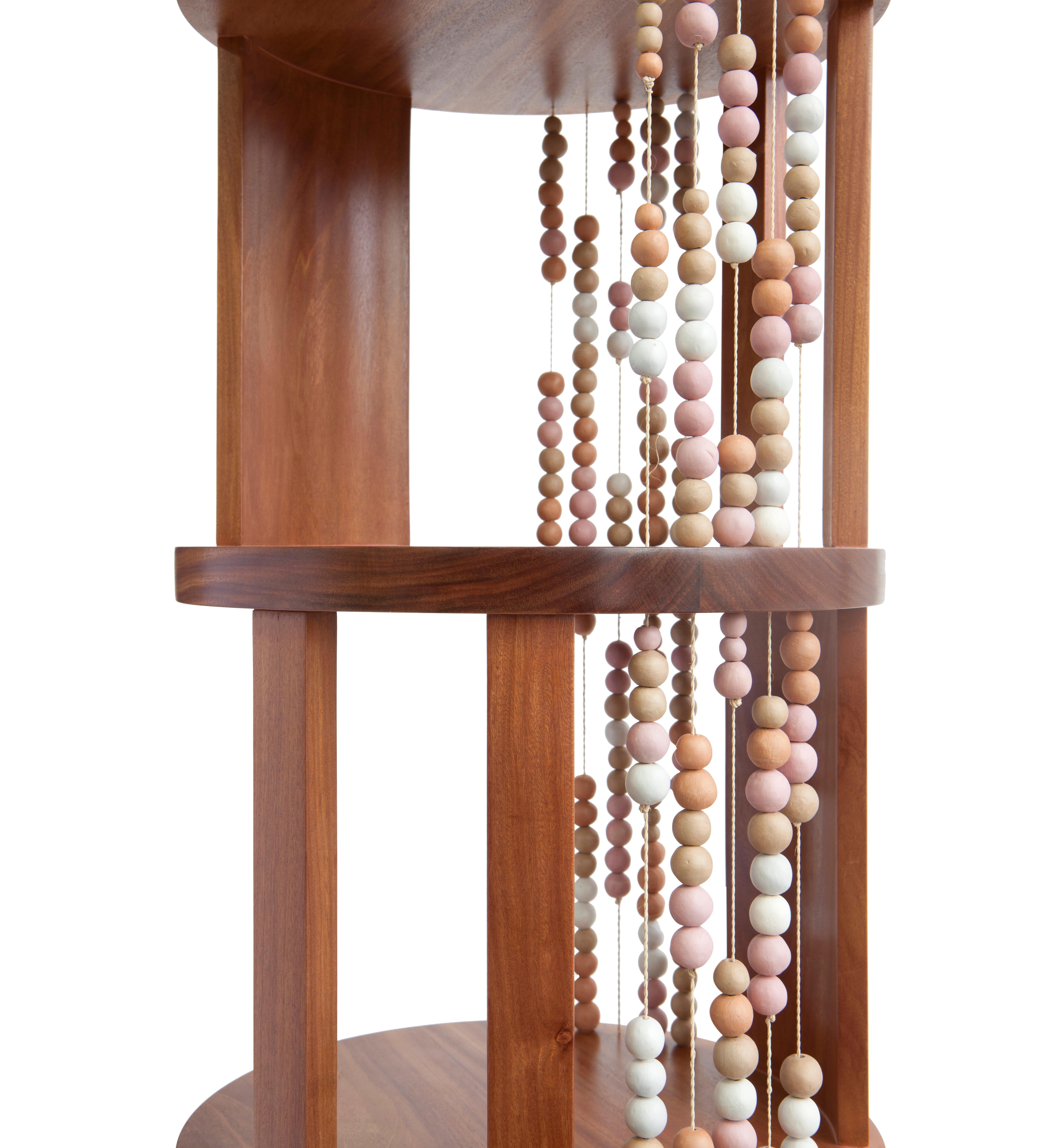 All the levels of this round bookcase, made of cabreuva hardwood, are permeated by buriti palms yarns with ceramic beads, creating different compositions depending on the angle we look at it. All the soft colored shades of the ceramic come from the