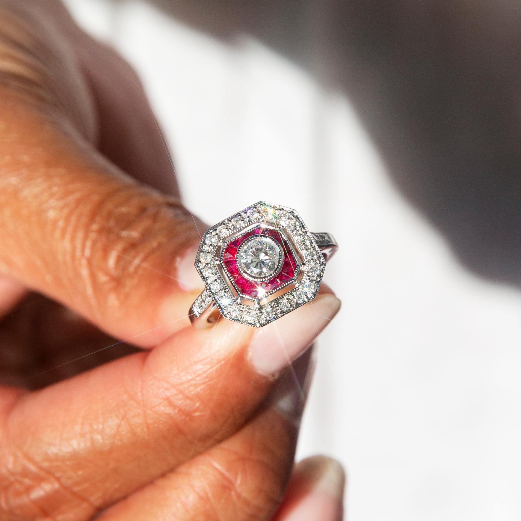 Crafted in 18 carat white gold, this stunning art deco-inspired halo ring features a gorgeous certified 0.38 carat round brilliant cut diamond encompassed by custom cut red rubies totalling 0.55 carats and an enchanting halo of glittering round