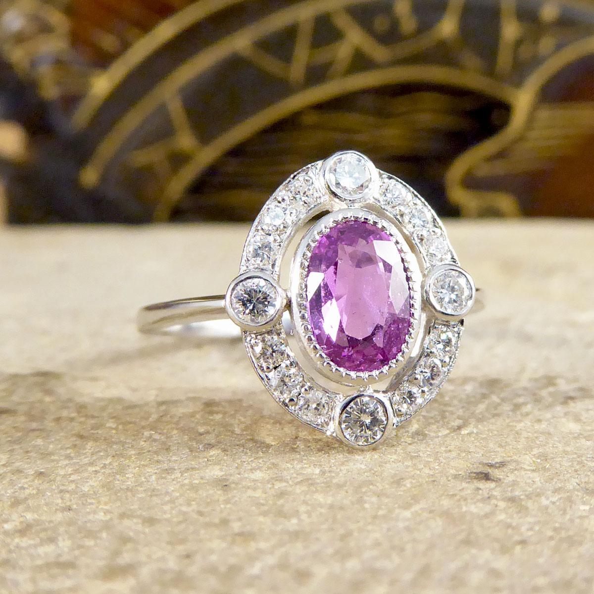 This stunning Contemporary ring has been made to resemble an Art Deco style ring with its geometric style, halo and setting. It features a single central Oval Pink Sapphire stone weighing 1.05ct in a milgrain rub over setting, surrounded by 16