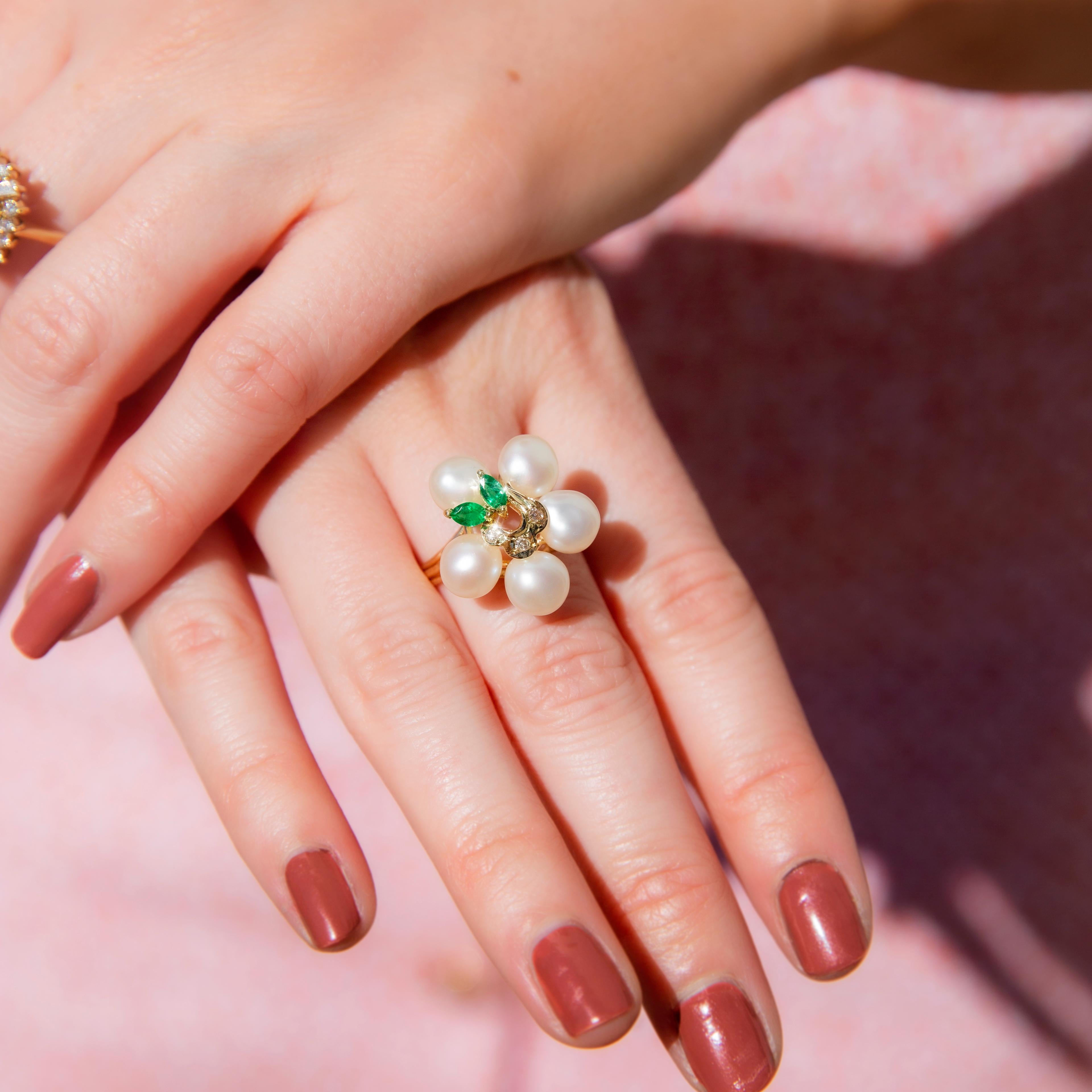 Crafted with love and affection in 12 carat yellow gold, this lovely contemporary ring features an elegant flower cluster of three central round brilliant cut diamonds, two offset marquise cut deep green emeralds and five gorgeous surrounding