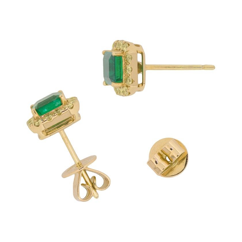 These stunning earrings feature luscious green emeralds and yellow diamonds. Each emerald weighs 0.65 carat, totalling to 1.29 carat. The Asscher cut emeralds are beautifully highlighted by a halo of fancy yellow diamonds. They have an estimated