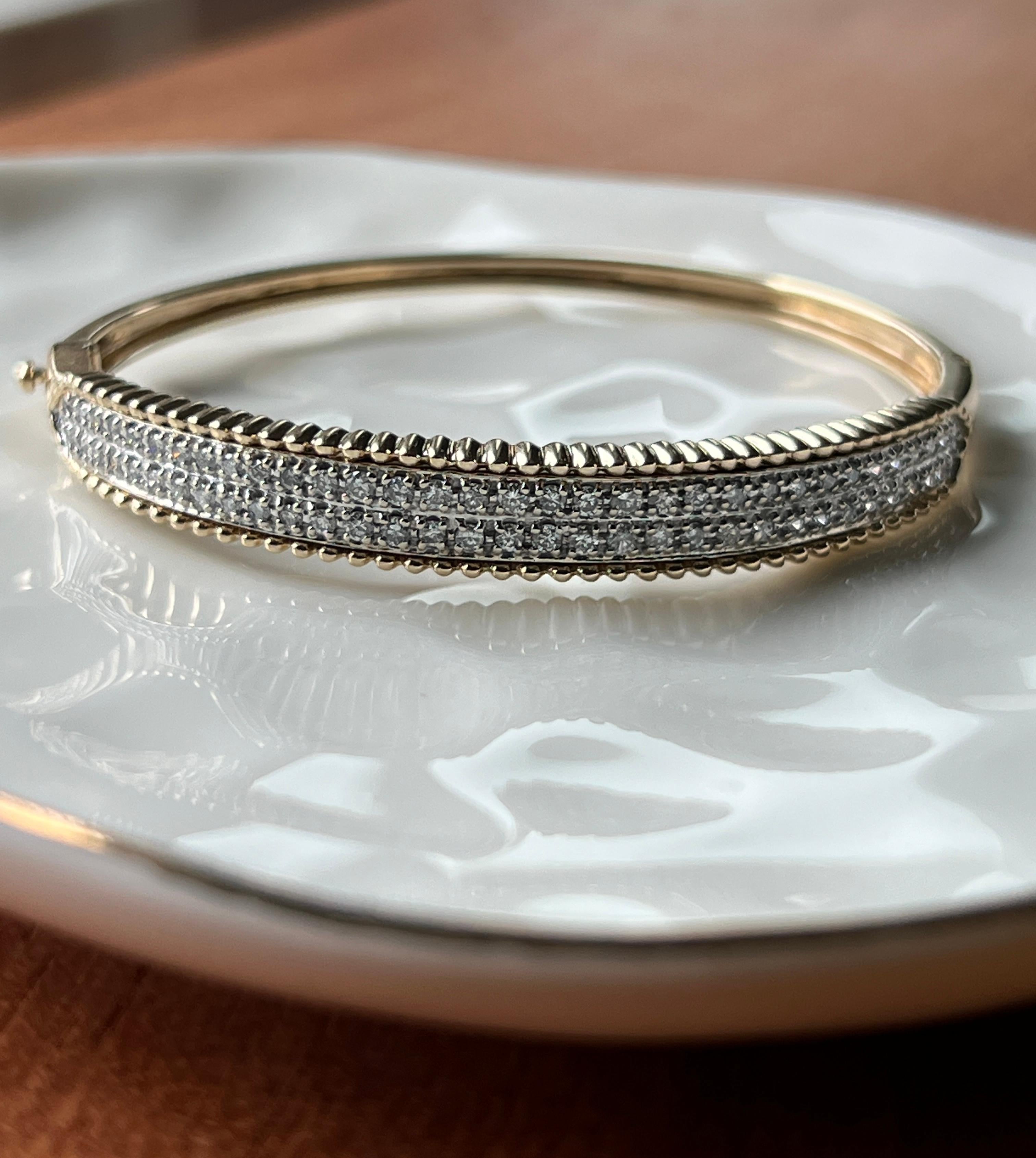 A refined blend of classic elegance and modern design, this contemporary bangle bracelet is crafted in 14 karat yellow and white gold and accented with a stunning row of sixty-six round brilliant-cut diamonds. The diamonds have a total approximate