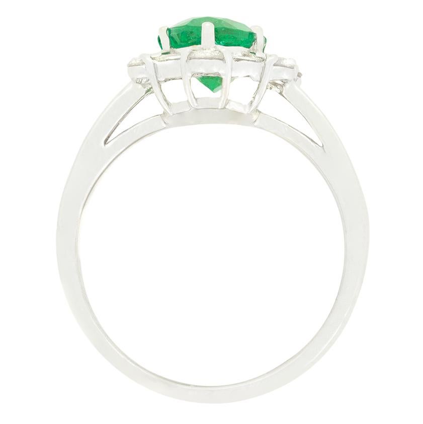 Im Mittelpunkt dieses schönen, modernen Clusterrings steht ein leuchtender Smaragd im Ovalschliff. Der intensiv grüne Stein wiegt 1,34 Karat und ist von einer Reihe von Diamanten im Baguetteschliff und runden Brillanten umgeben. Die abwechselnd