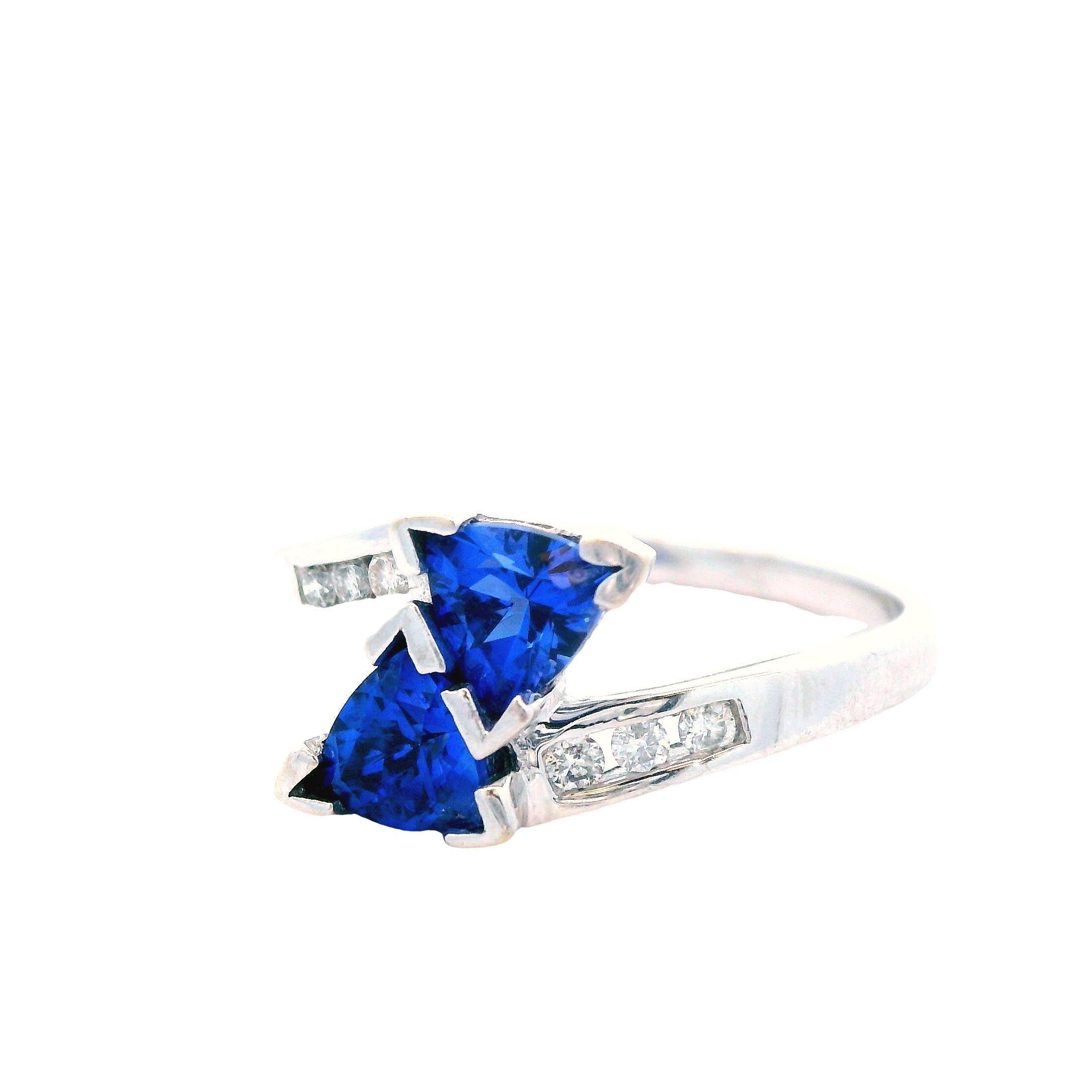 This is an absolutely stunning ring in 14k white gold featuring diamond accents and two breathtaking trillion cut tanzanite center stones! The ring has an elegant overlapping style that puts the tanzanite on perfect display, front and center. The