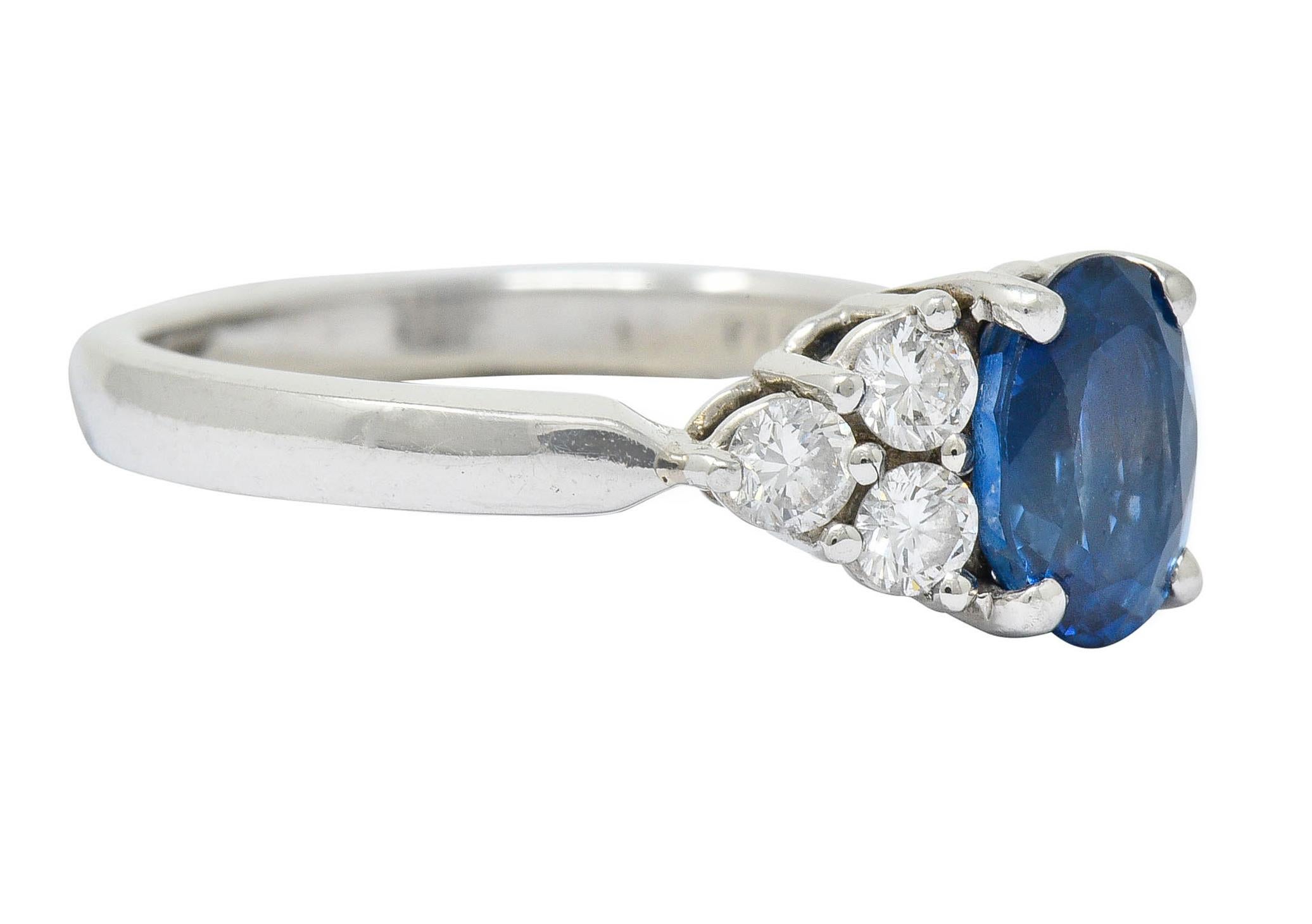 Centering an oval cut sapphire weighing approximately 1.16 carats

Transparent with enticing medium-light denim blue color

Flanked by triads of round brilliant cut diamonds at shoulders

Weighing in total approximately 0.35 carat with G/H color and