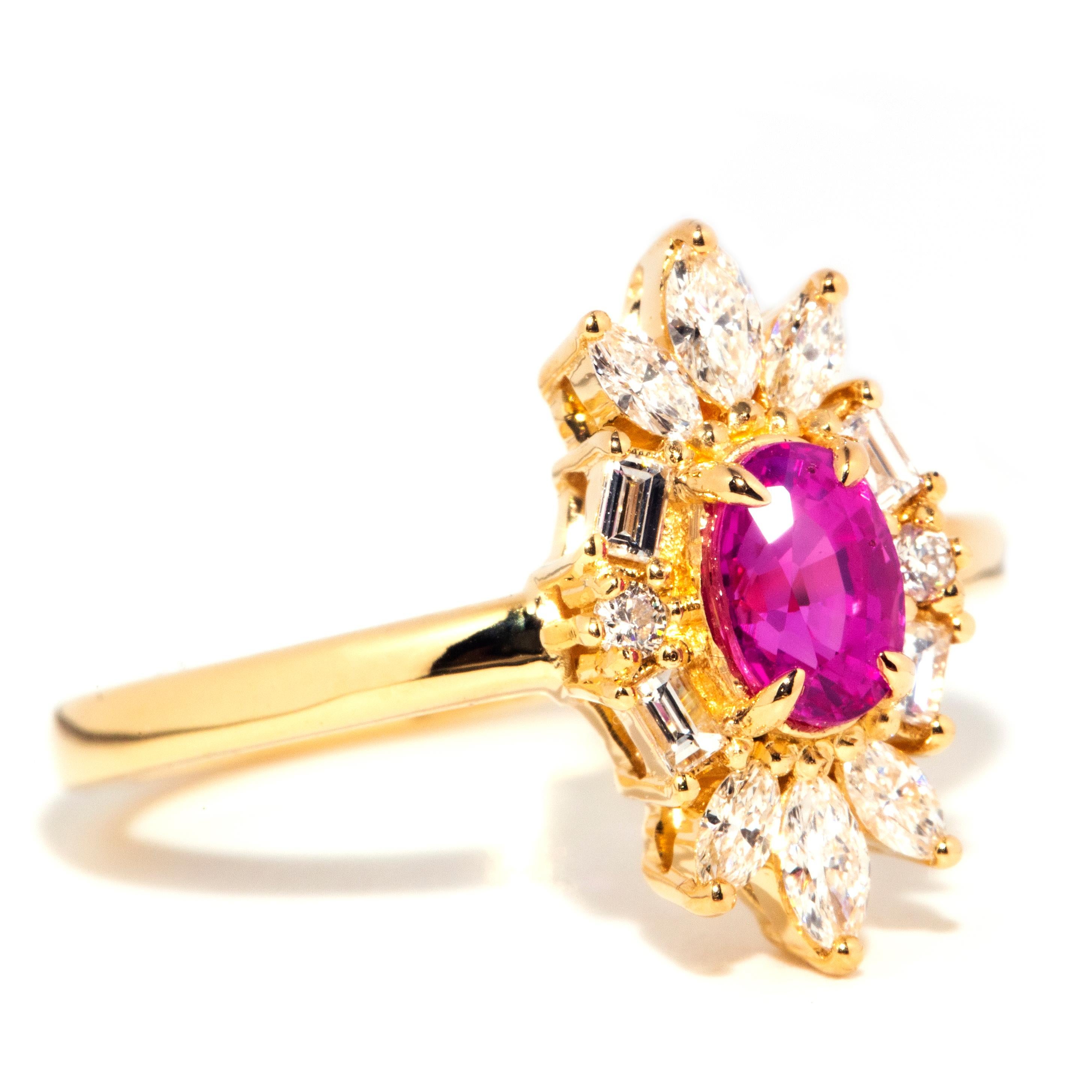 Lovingly crafted in 18 carat yellow gold, this gorgeous contemporary ring features a fabulous oval cut natural bright intense deep pink sapphire at the centre of a captivating elongated starburst cluster of marquise, baguette, and round brilliant