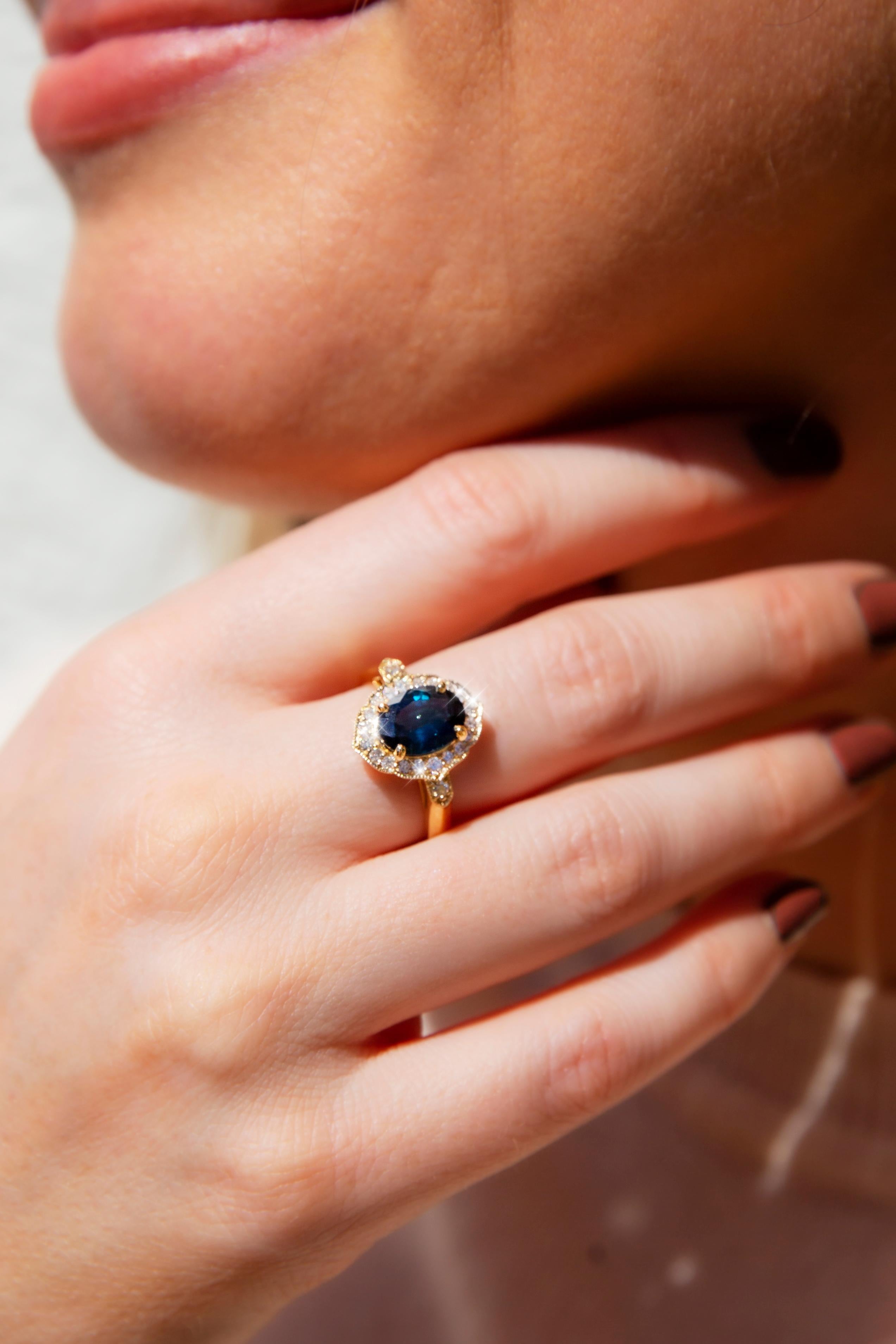 Crafted in 18 carat gold, this gorgeous contemporary ring features a decadent halo setting with an alluring oval Australian teal sapphire with a blue secondary colour, encompassed by a halo border of shimmering round brilliant cut diamonds. The