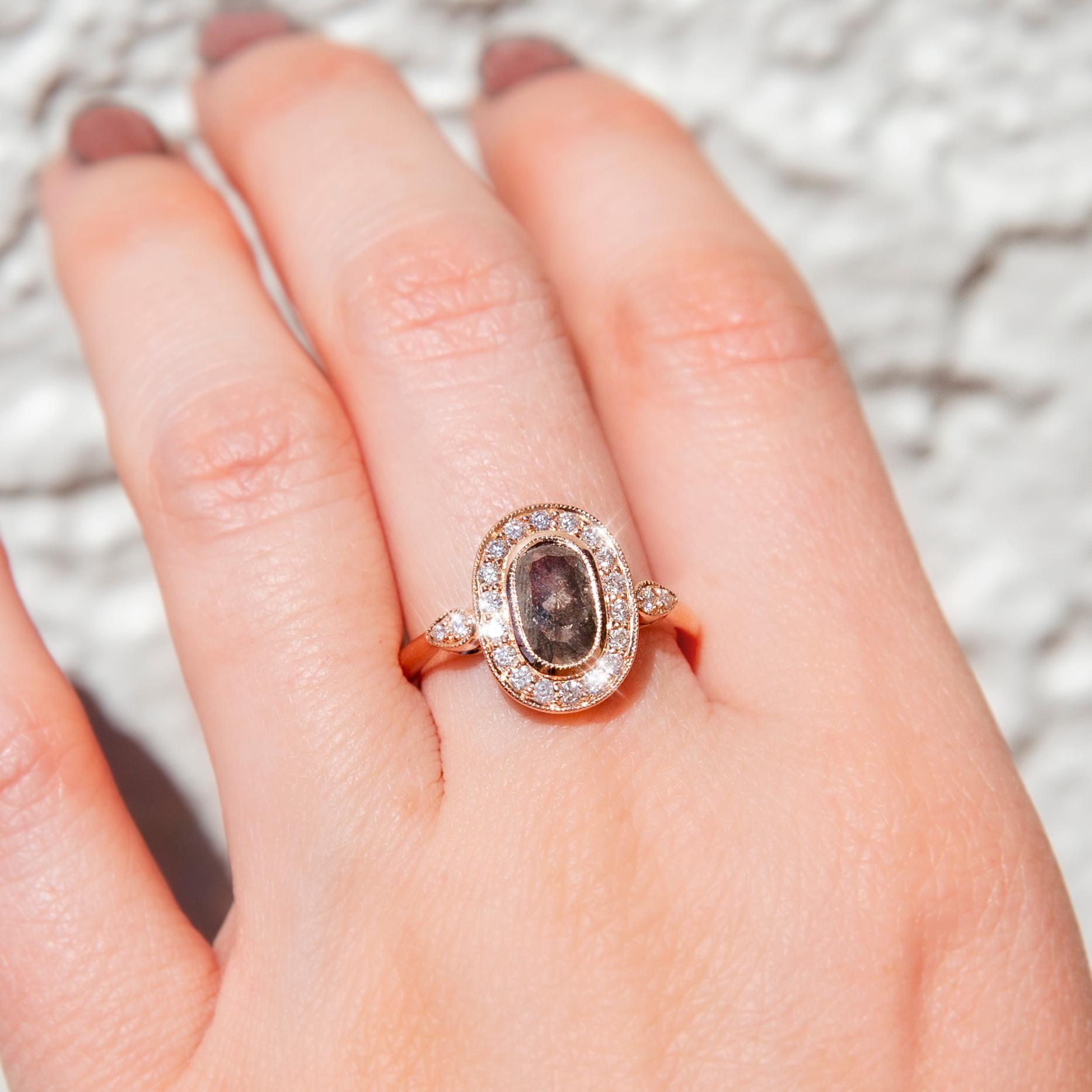 Lovingly crafted in 18 carat rose gold, this stunning contemporary ring features a gorgeous oval rose cut 1.13 carat 'salt and pepper' diamond in an elegant millegrain setting with a halo of bead set round brilliant diamonds shimmering in unity. We