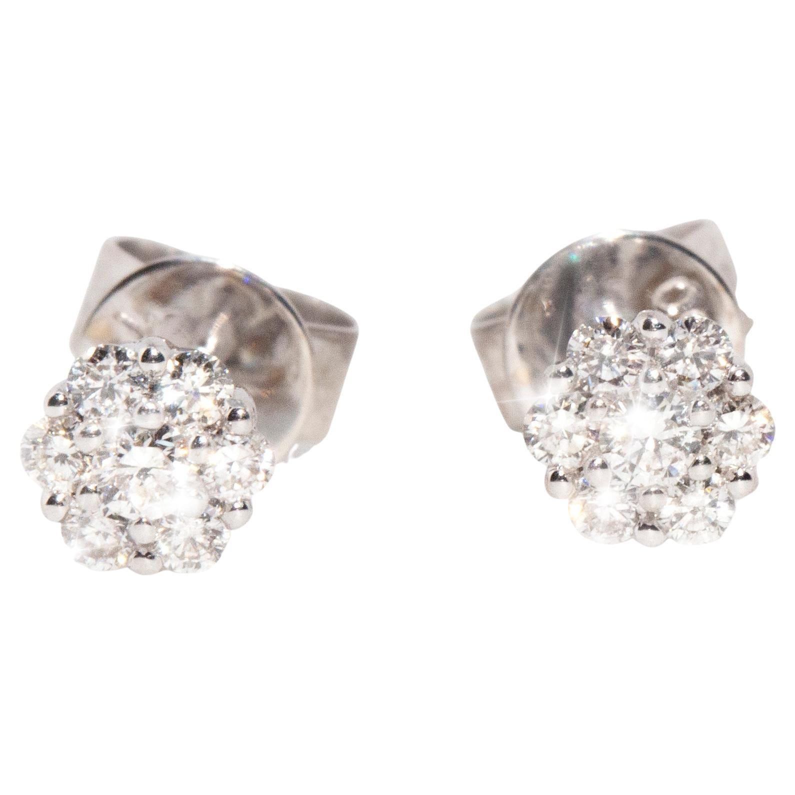 Crafted with love in 18 carat white gold, this lovely pair of vintage stud earrings each feature a delightful flower cluster with seven round brilliant cut diamonds glistening in unison on butterfly post backings. We have named these elegant