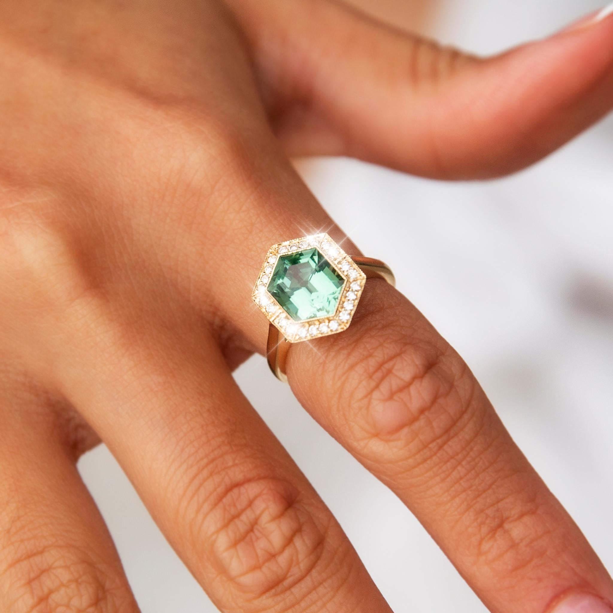 Crafted with love and care in 18 carat yellow gold, this lovely contemporary ring features a gorgeous mint green hexagonal cut tourmaline at the centre of an elegant basket setting with a gleaming border of bead set round brilliant and princess cut