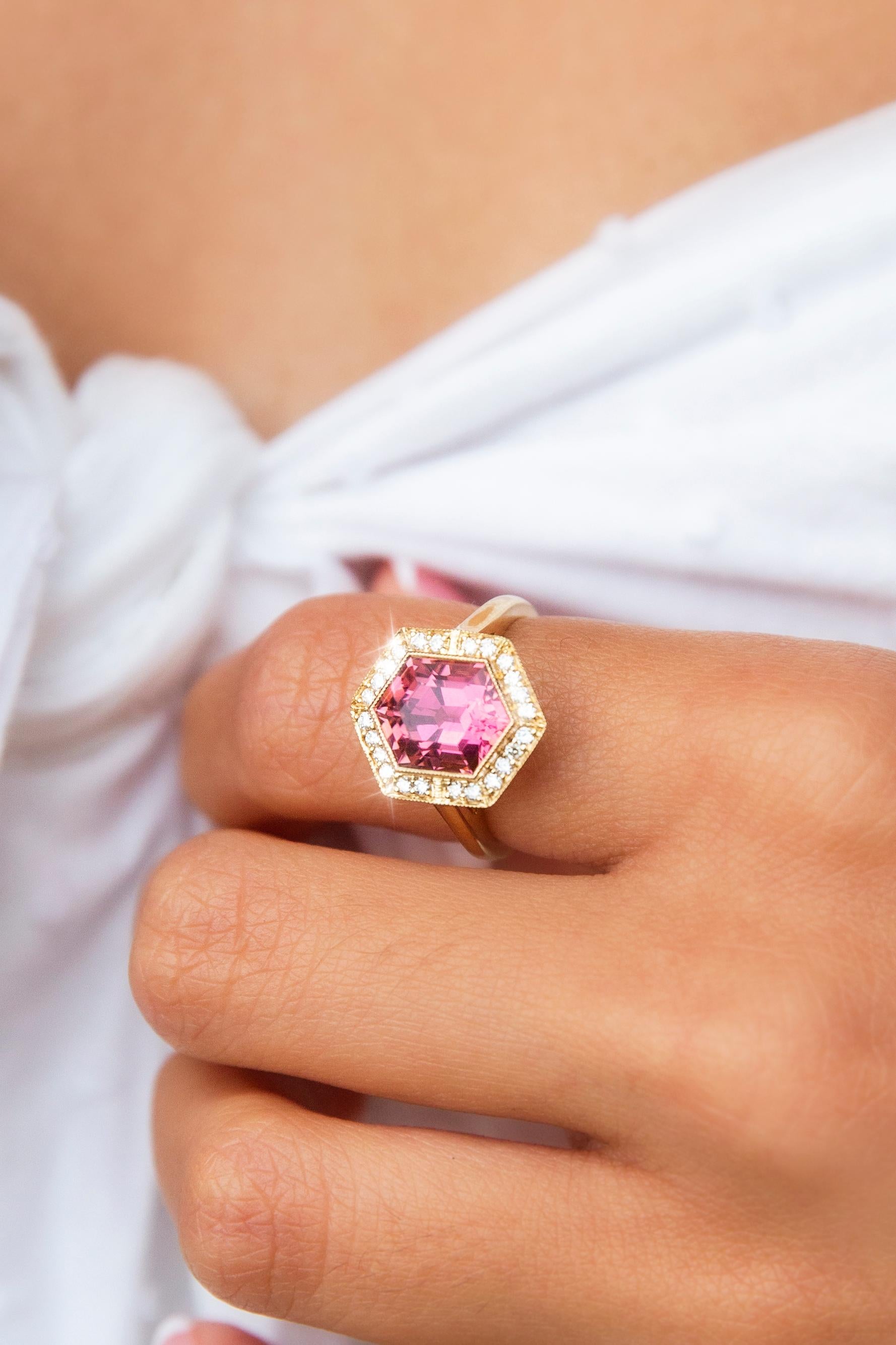 Crafted with love and care in 18 carat yellow gold, this breathtaking contemporary ring features a gorgeous peach-pink hexagonal cut tourmaline at the centre of an elegant basket setting with a shimmering border of bead set round brilliant cut
